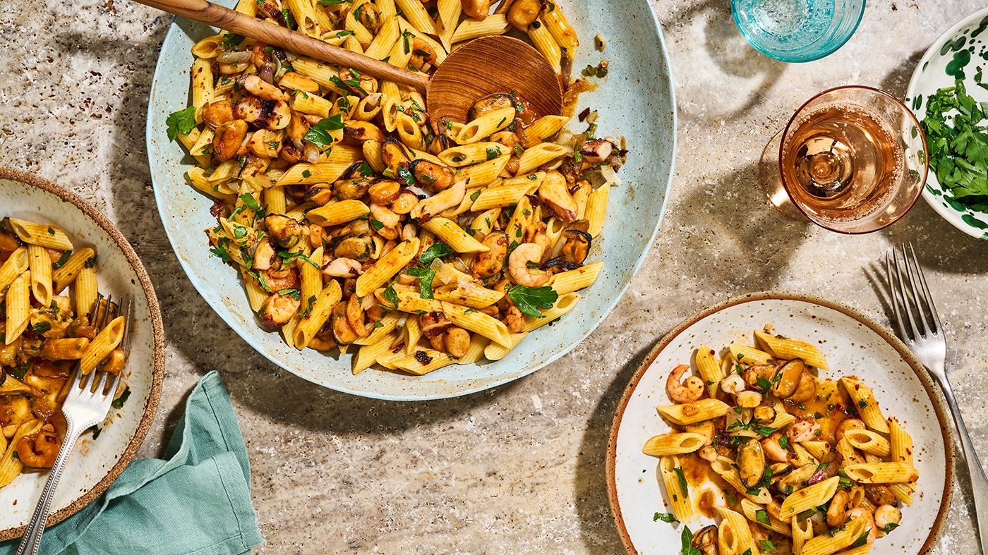 Rezept für Meeresfrüchte-Penne mit Anis Große Schale und kleine Teller gefüllt mit Nudeln und Meeresfrüchten