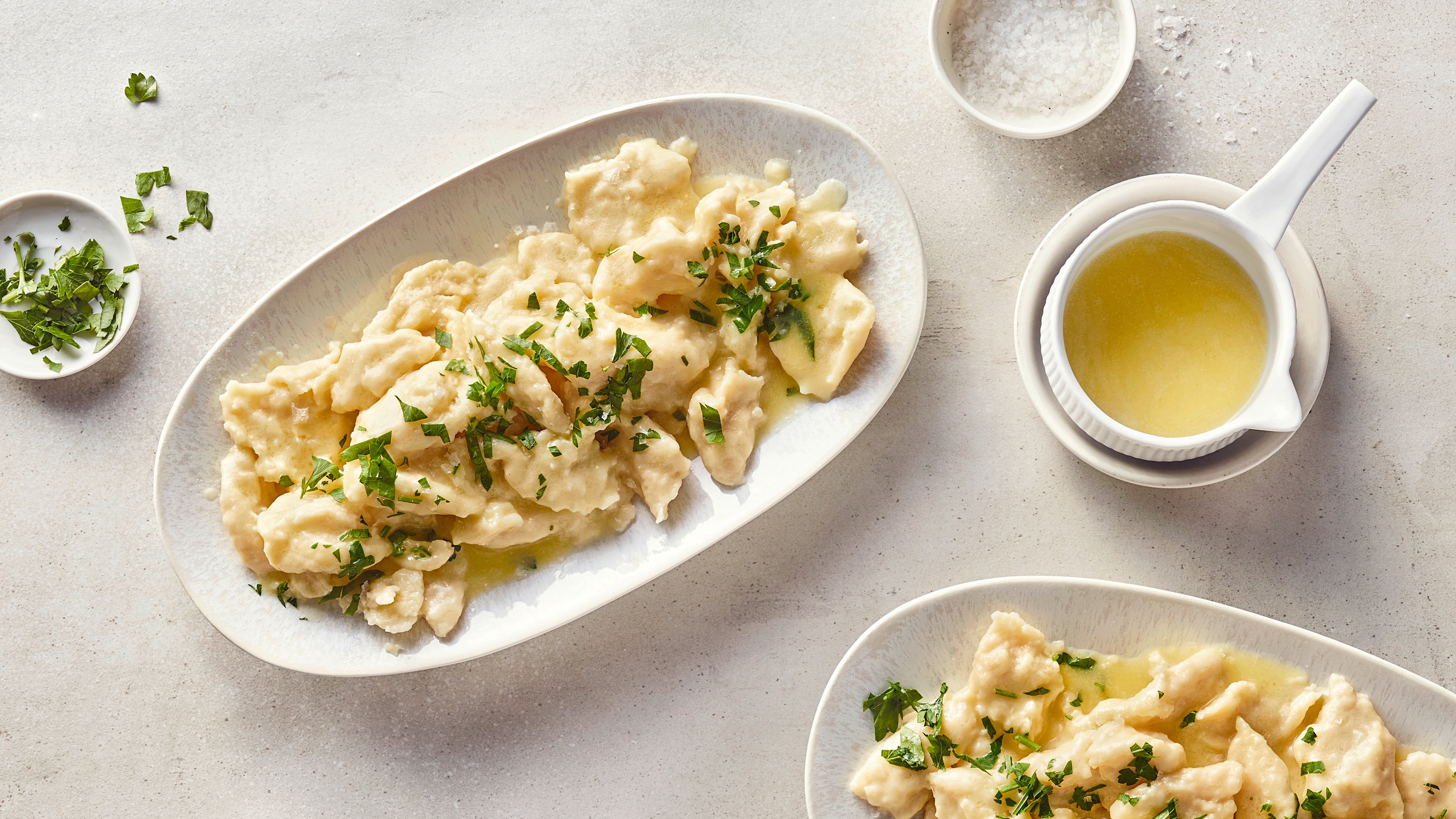 Klößchen-Rezept für Mehlspatzen Zwei ovale Teller mit hellen Teigklößchen in klarer Butter, getoppt mit frisch gehackter Petersilie