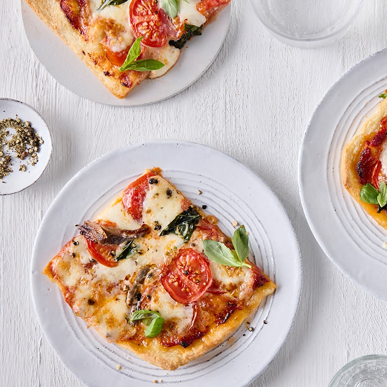 Drei runde, weiße Teller mit jeweils einem belegtem Pizzastück.