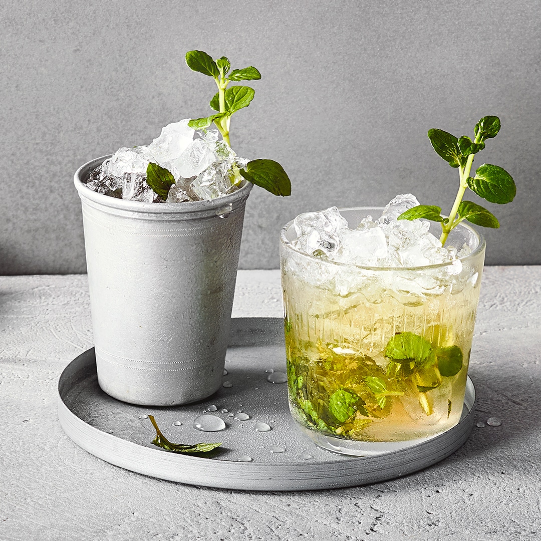 Gläser gefüllt mit Eis und gelblicher Flüssigkeit, garniert mit grünen Kräutern