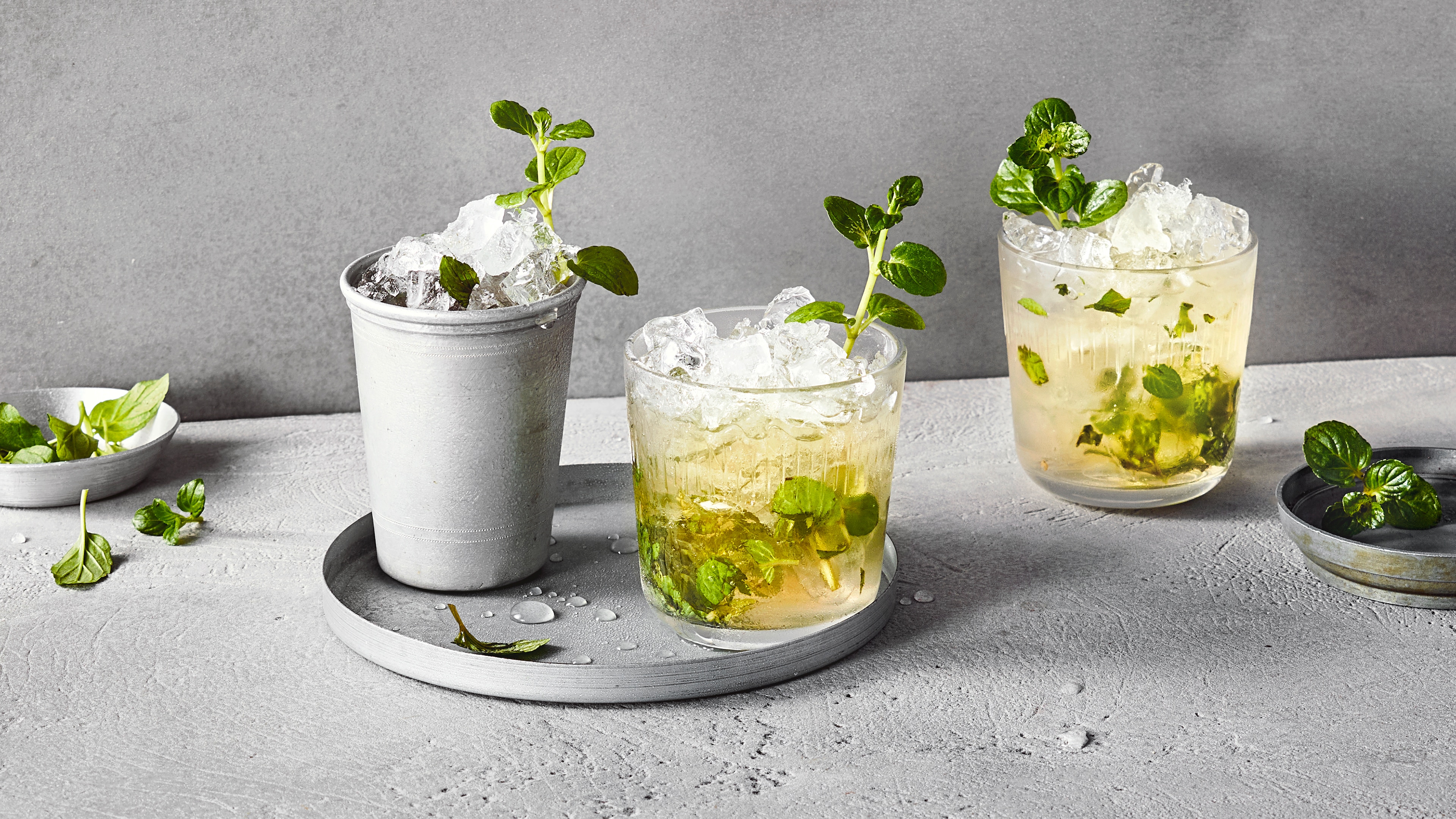 Gläser gefüllt mit Eis und gelblicher Flüssigkeit, garniert mit grünen Kräutern