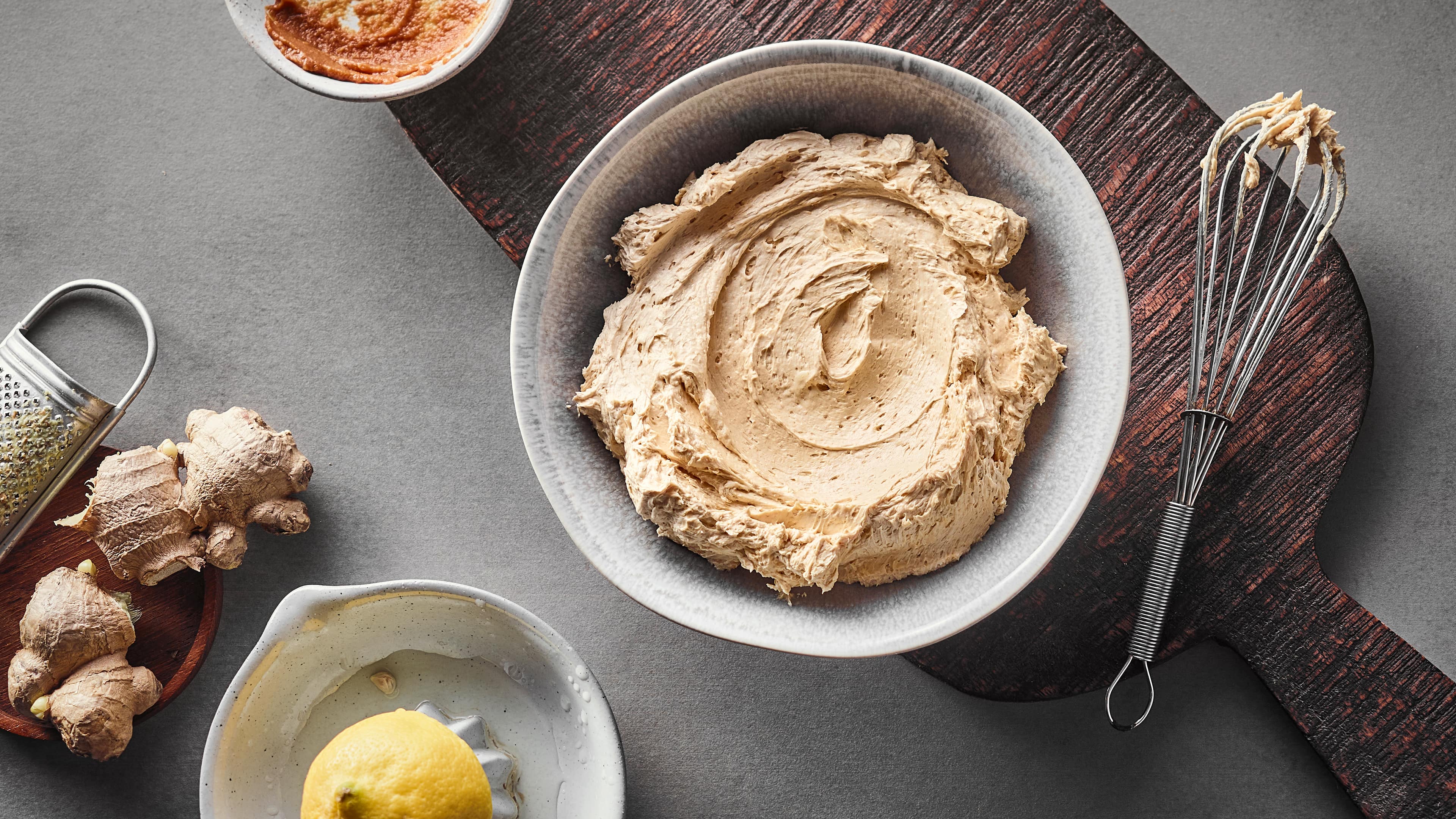 Rezept für würzige Miso-Butter Cremige, luftige hellbraune Butter in einer Schale auf einem rustikalen Holzbrett, daneben ein Schneebesen