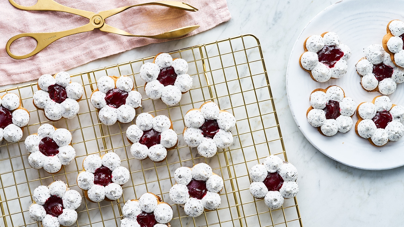 Rezept für Mohn-Kirsch-Ringe Ein Gitter mit blumenförmigen Keksen mit weißer Glasur und einem roten Gelee-Punkt in der Mitte