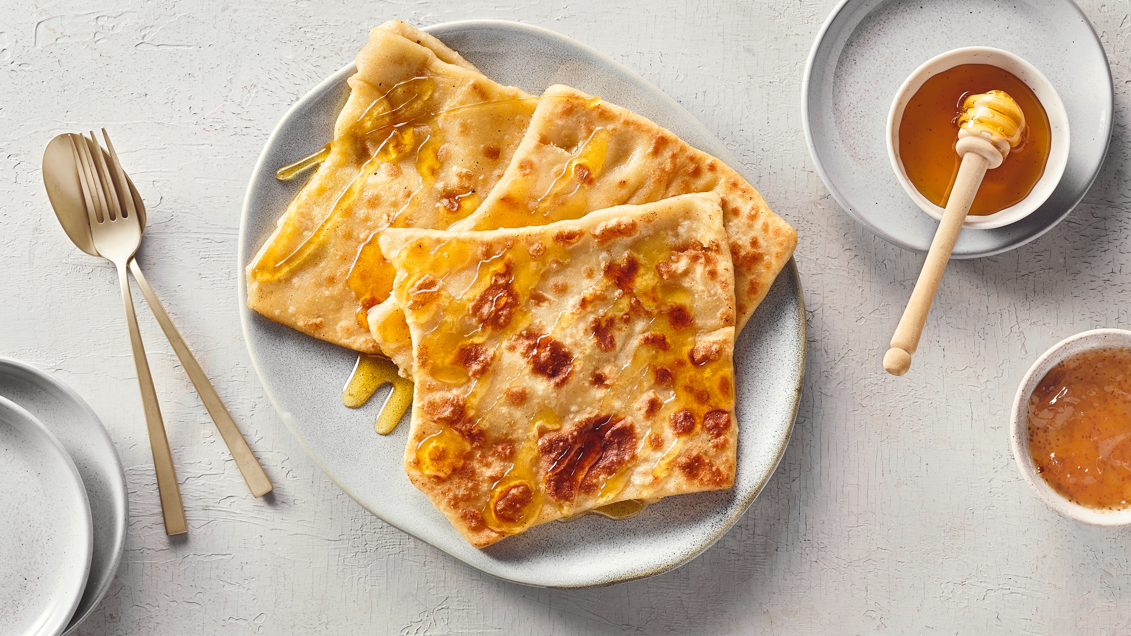 Ein Teller mit drei flachen, goldbraunen Teigstücken, die mit glänzendem Honig überzogen sind.