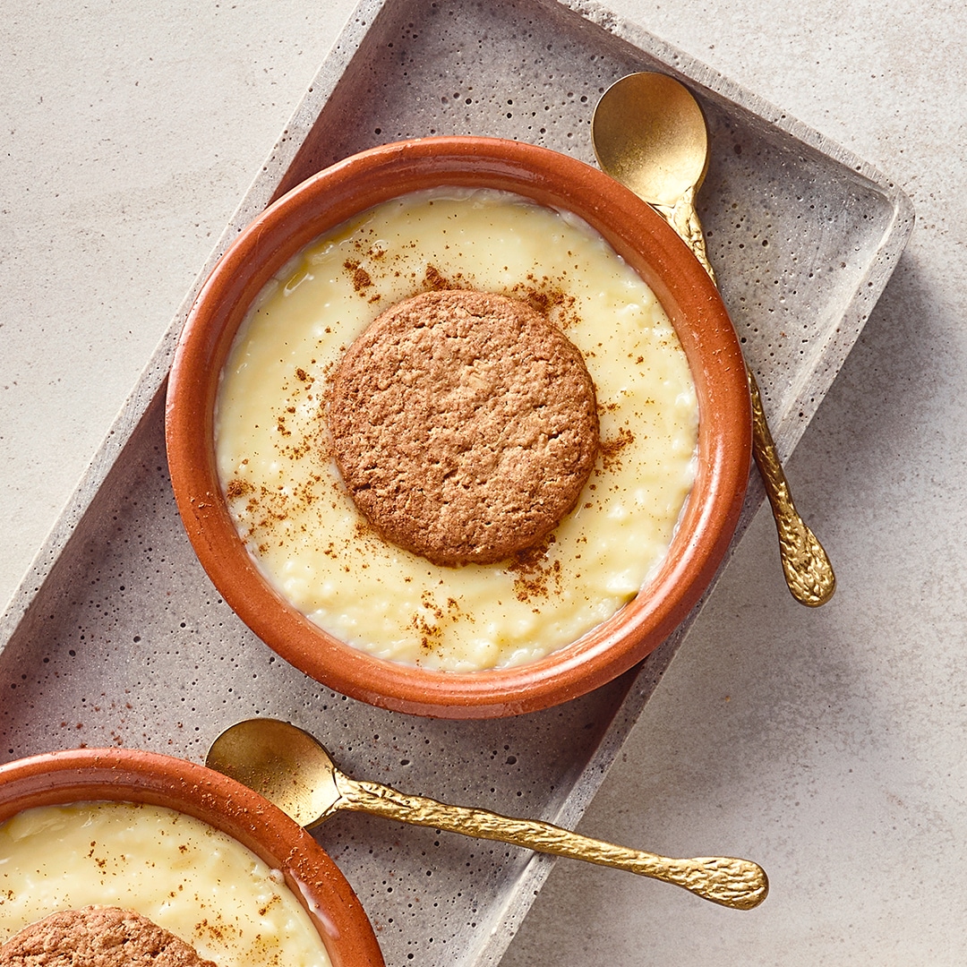 Kleine Dessertschälchen aus Ton mit einer hellen Creme, getoppt mit knusprigen Keksen und bestreut mit Zimt