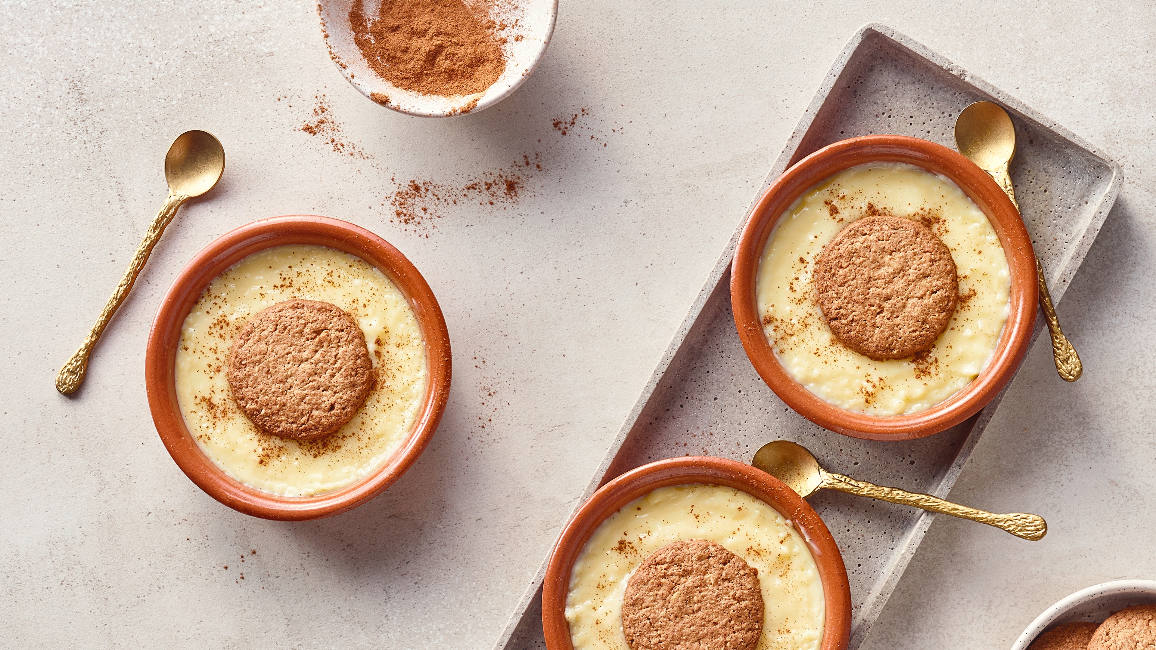 Kleine Dessertschälchen aus Ton mit einer hellen Creme, getoppt mit knusprigen Keksen und bestreut mit Zimt