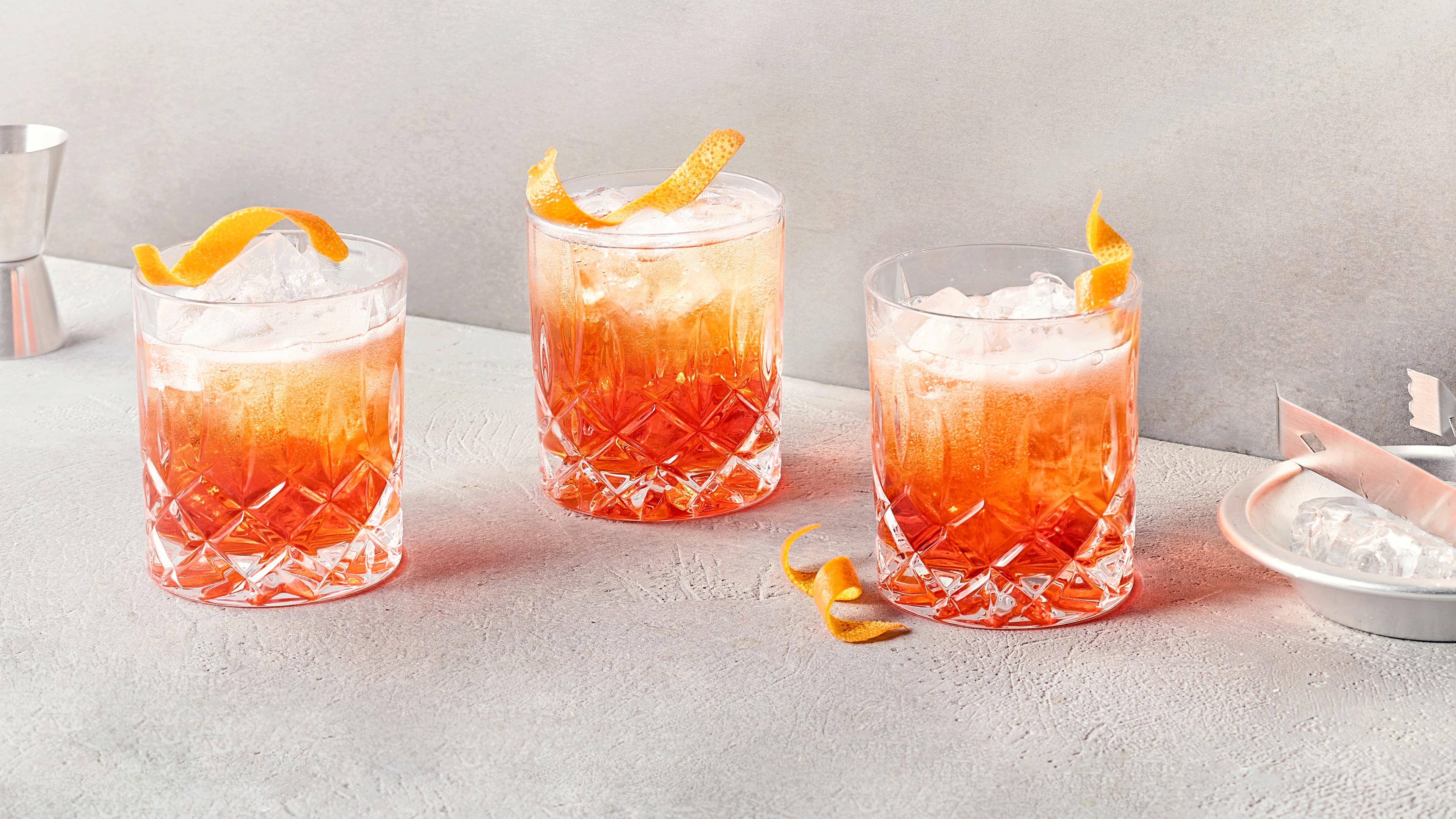 Ein Glas mit orangefarbenem Getränk auf Eis, garniert mit einer gedrehten Zitronenschale.