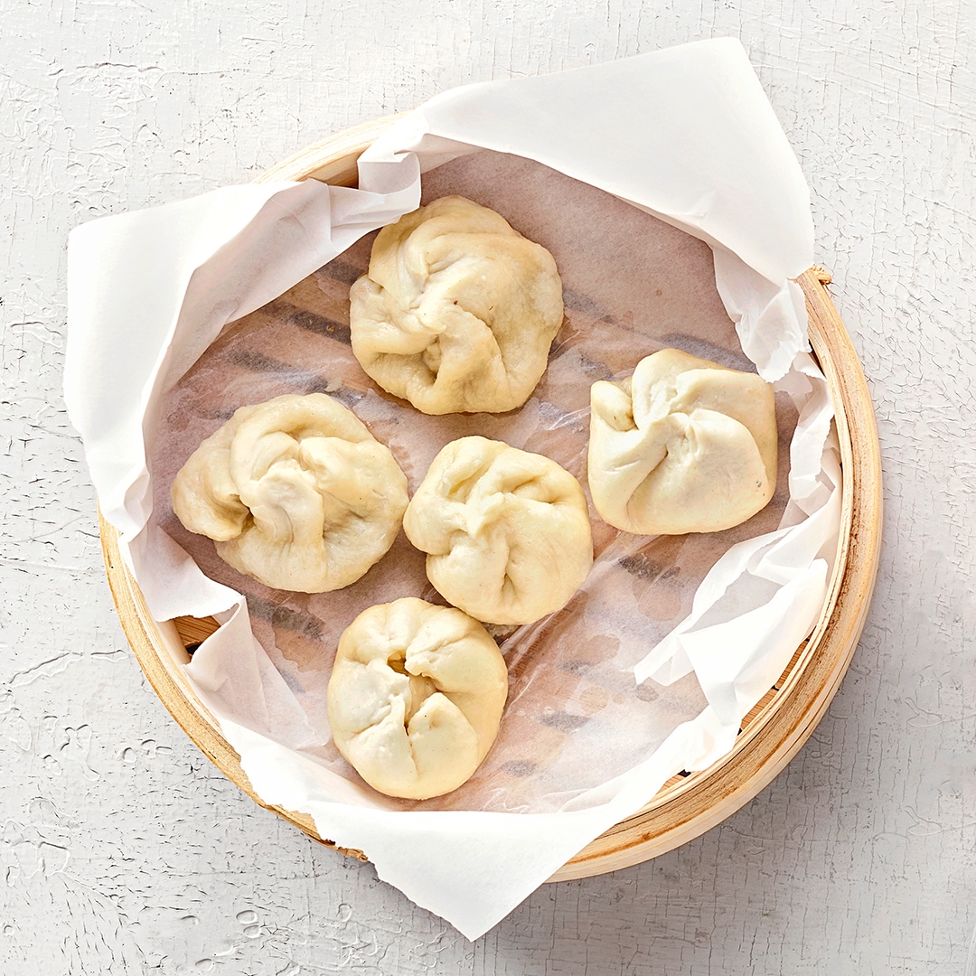 Kordschale mit gefüllten Teigtaschen. Daneben Essspieße und Sojasauce.