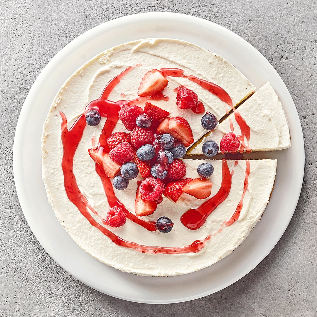 Cremiger runder Kuchen garniert mit Fruchtsoße, Himbeeren, Blaubeeren und Erdbeeren