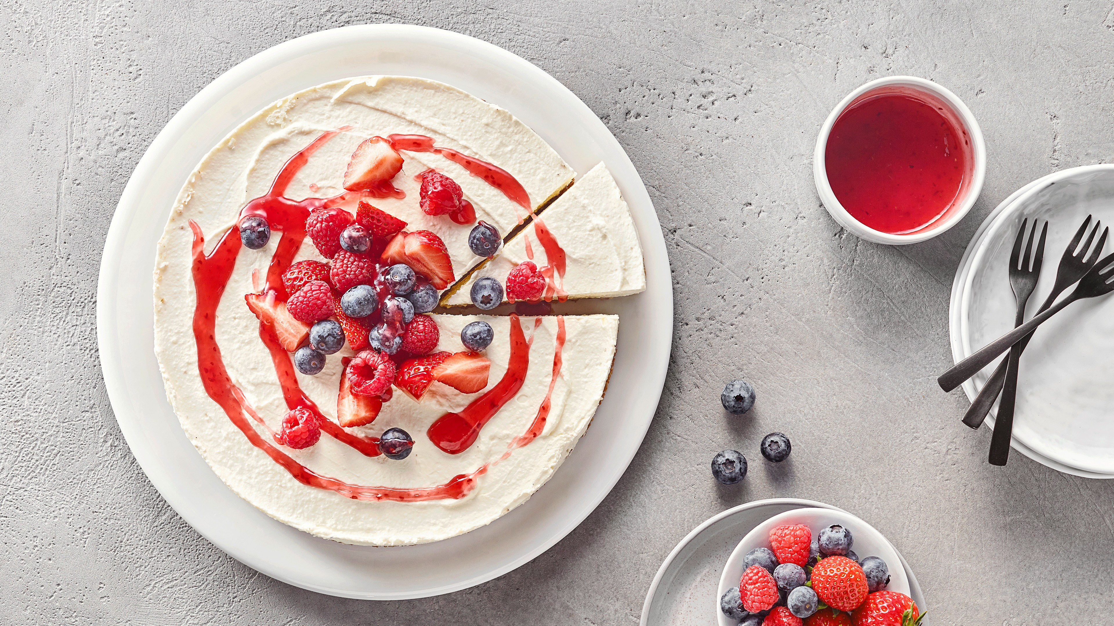 Cremiger runder Kuchen garniert mit Fruchtsoße, Himbeeren, Blaubeeren und Erdbeeren