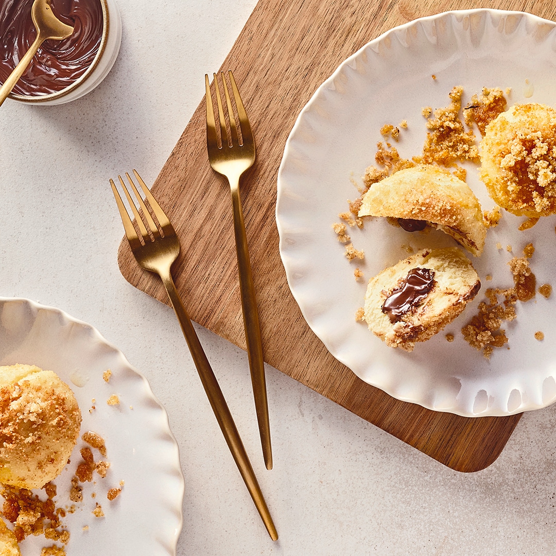 Helle, kleine klitschige Teigbällchen mit einem weichen Nougatkern, getoppt mit gehackten Nüssen, auf geriffelten Tellern