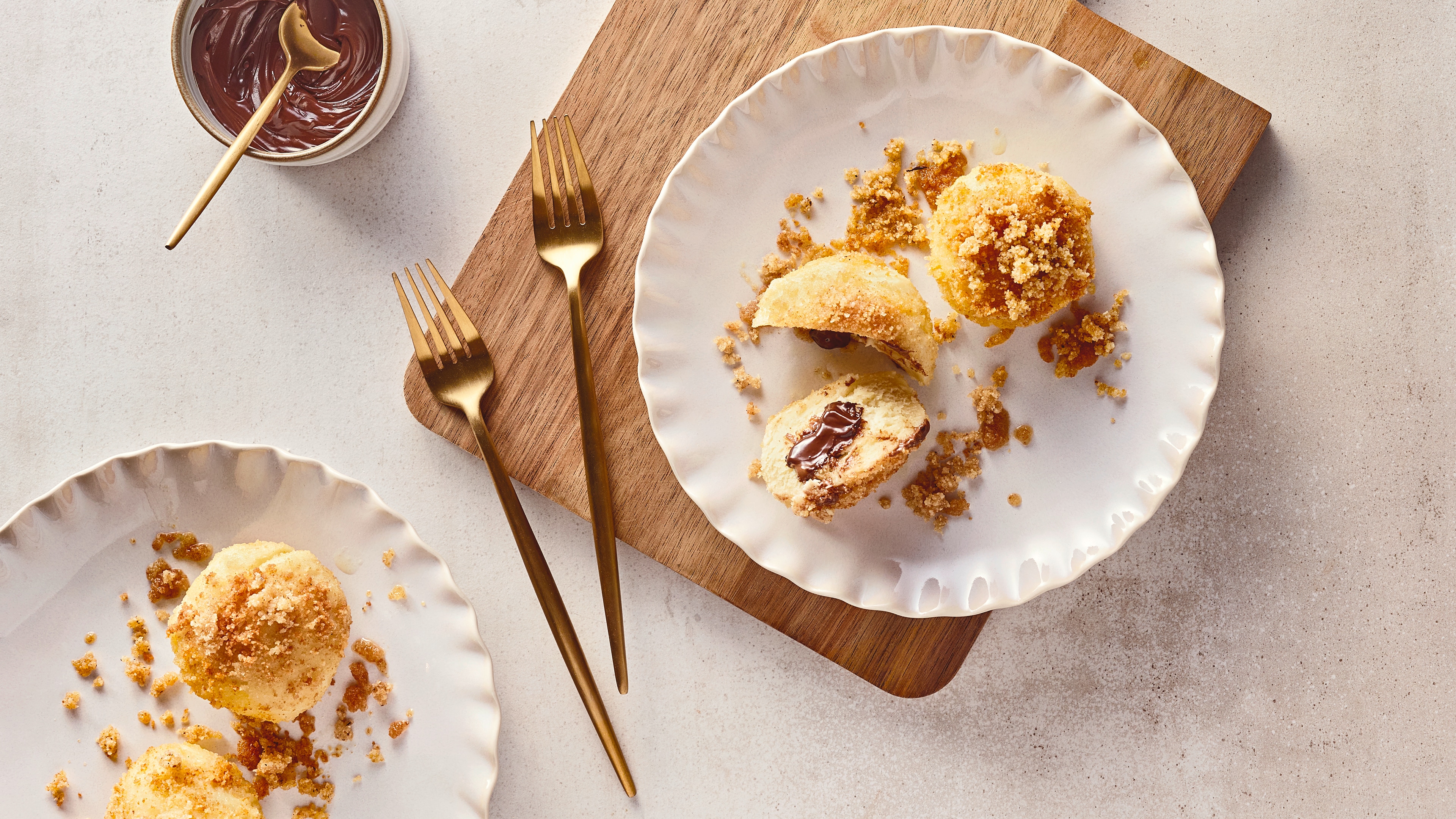 Rezept für Nugatknödel Helle, kleine klitschige Teigbällchen mit einem weichen Nougatkern, getoppt mit gehackten Nüssen, auf geriffelten Tellern