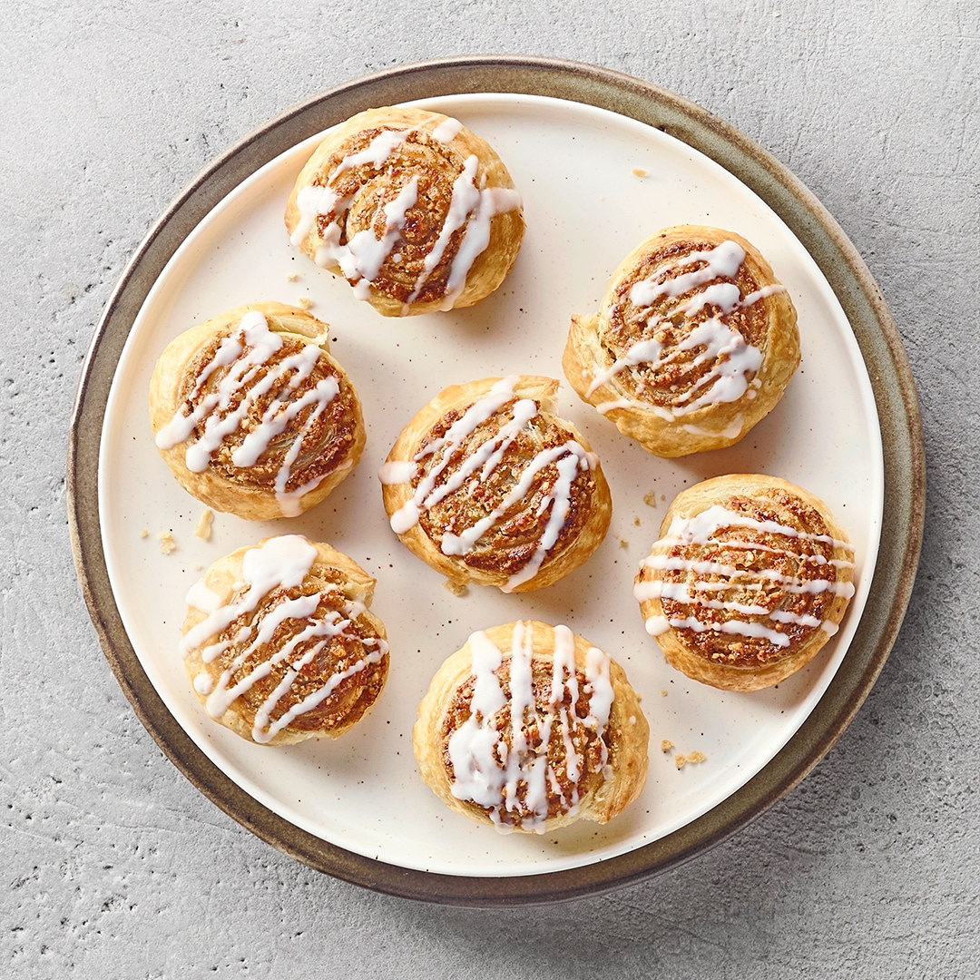 Ein Teller mit einer hellen Zimtschnecke, überzogen mit weißem Zuckerguss und braunen Zimtsplittern.