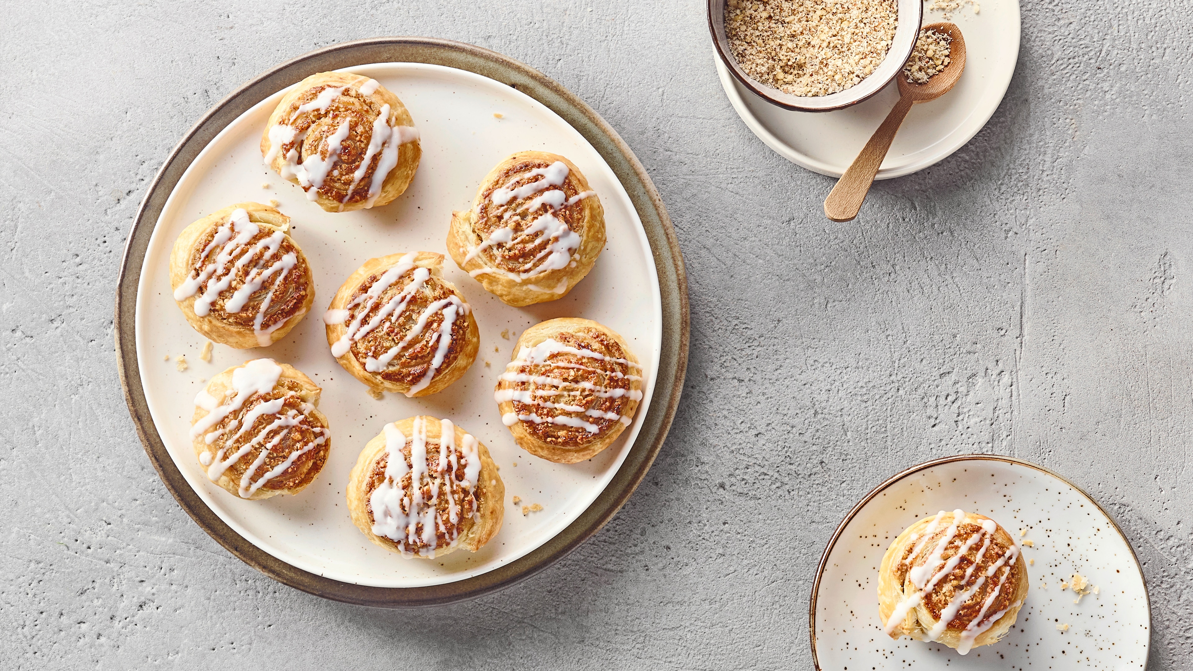 Ein Teller mit einer hellen Zimtschnecke, überzogen mit weißem Zuckerguss und braunen Zimtsplittern.