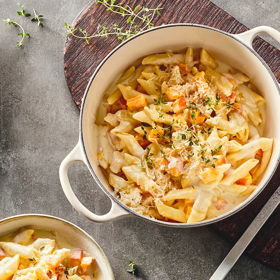 Ein Topf mit cremiger Penne in heller Soße mit Kürbisstückchen, getoppt mit geriebenem Käse