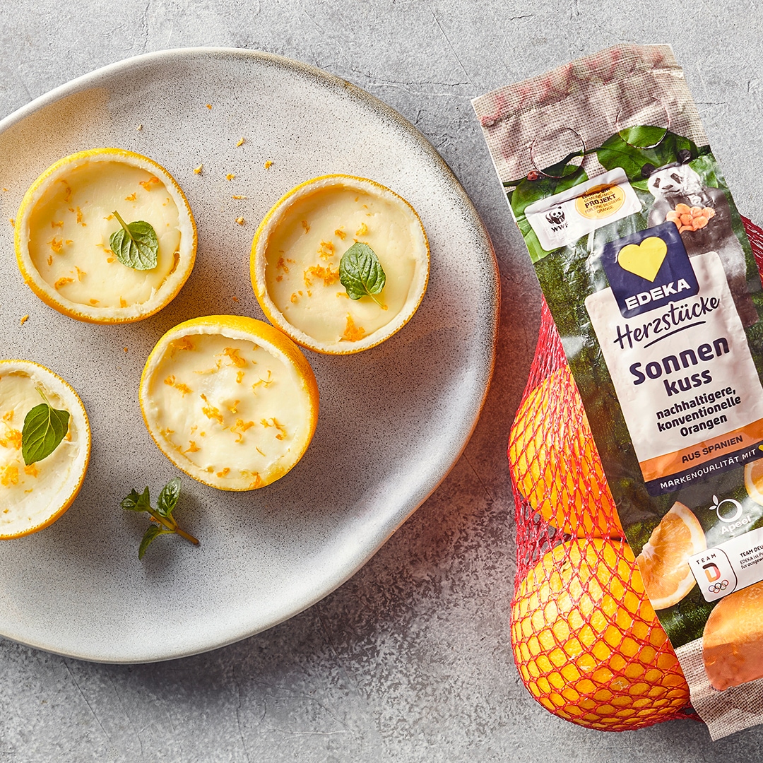 Ein Teller mit Zitronenhälften, gefüllt mit weißer Creme, garniert mit Minzblättern und feinen gelben Zesten