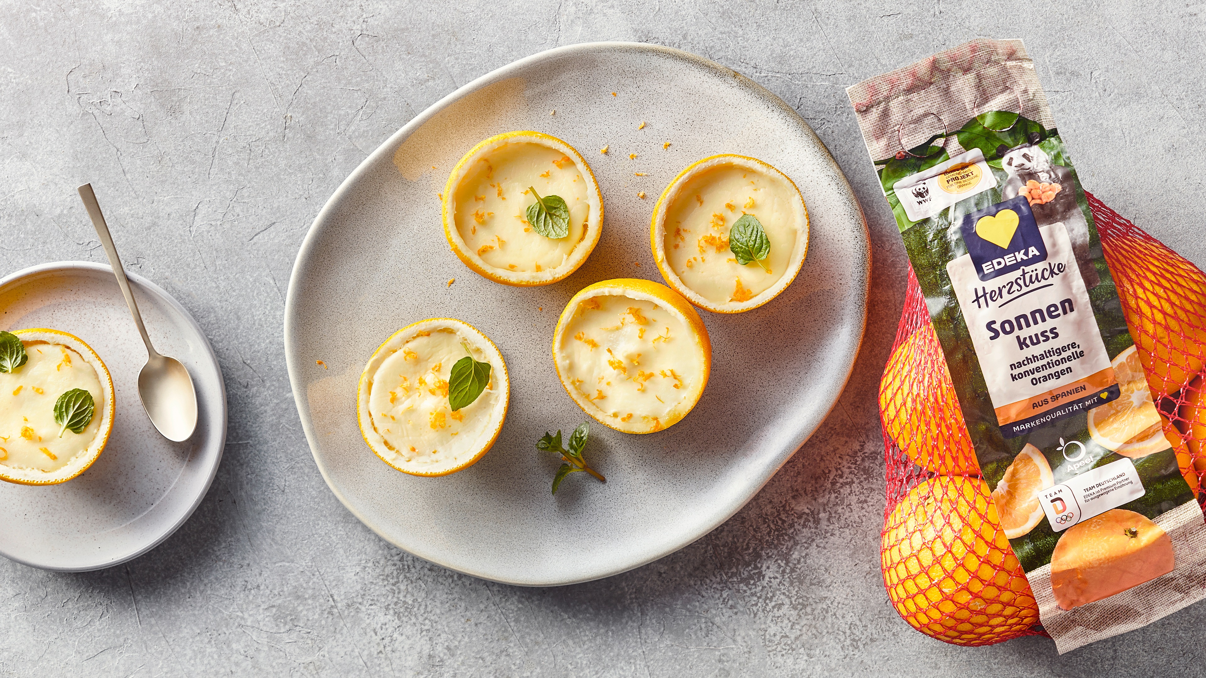 Ein Teller mit Zitronenhälften, gefüllt mit weißer Creme, garniert mit Minzblättern und feinen gelben Zesten