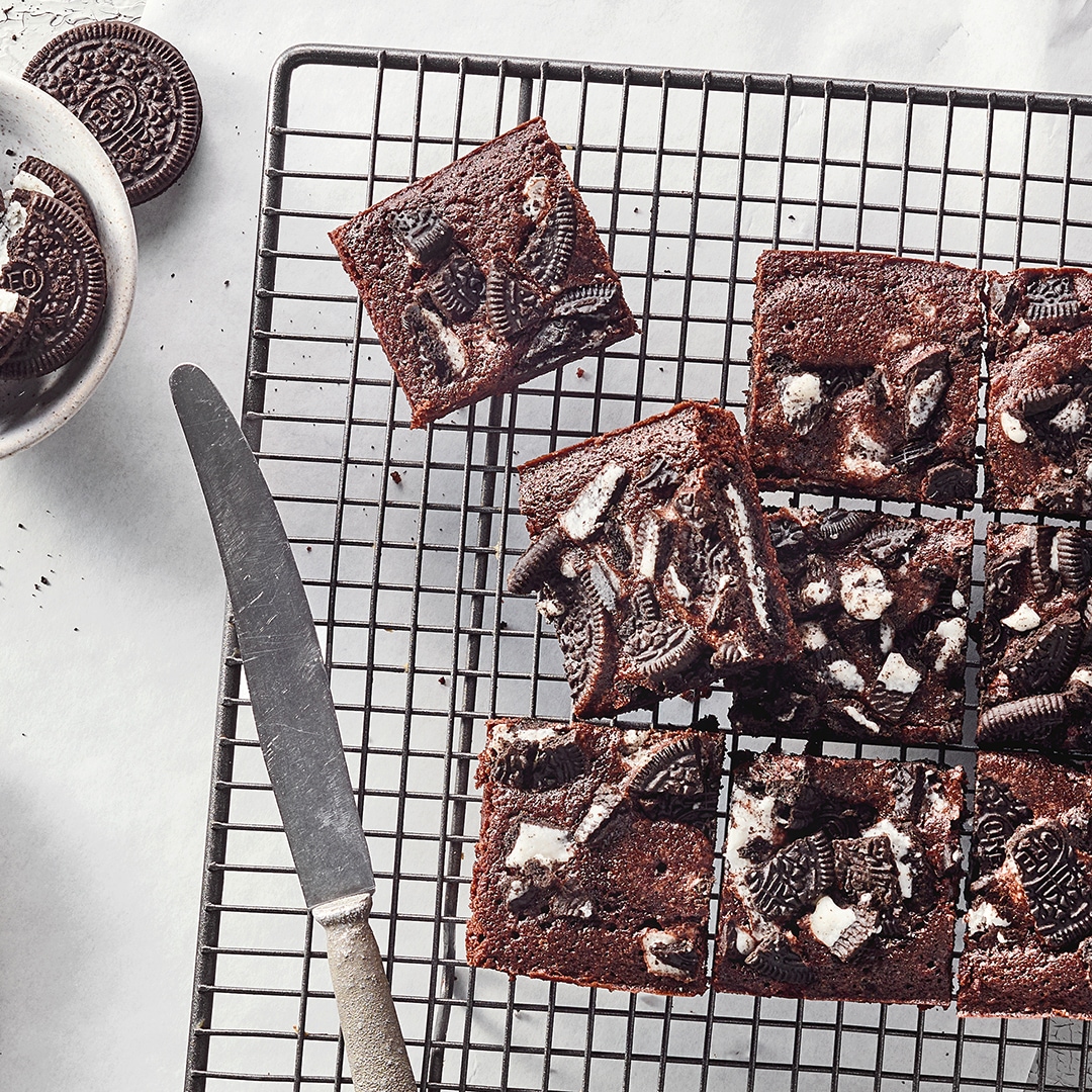Ein Gitter mit quadratischen Stücken dunklem Kuchen, darauf zerbrochene Kekse mit weißer Füllung, daneben Oreo-Kekse.