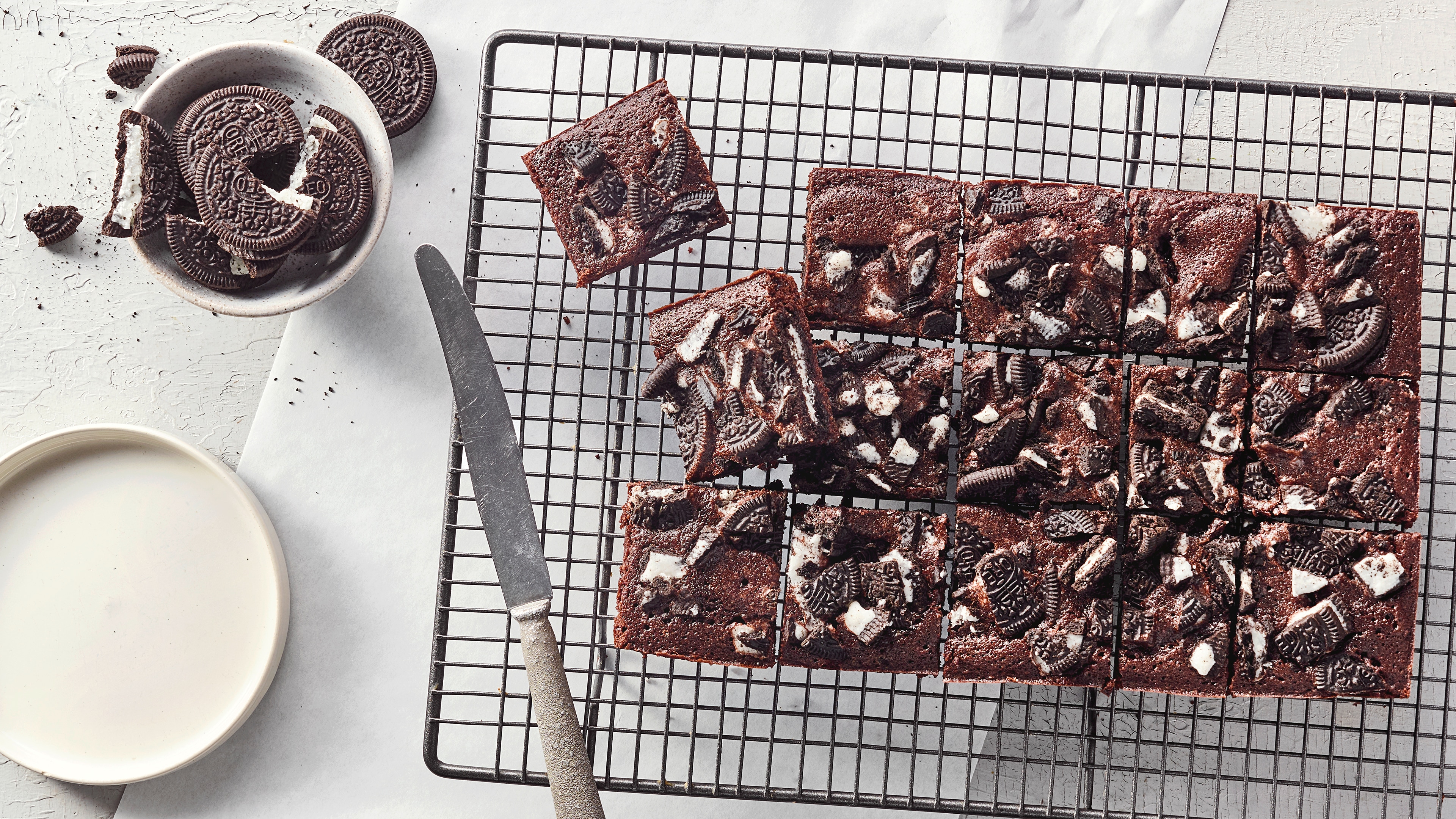 Ein Gitter mit quadratischen Stücken dunklem Kuchen, darauf zerbrochene Kekse mit weißer Füllung, daneben Oreo-Kekse.