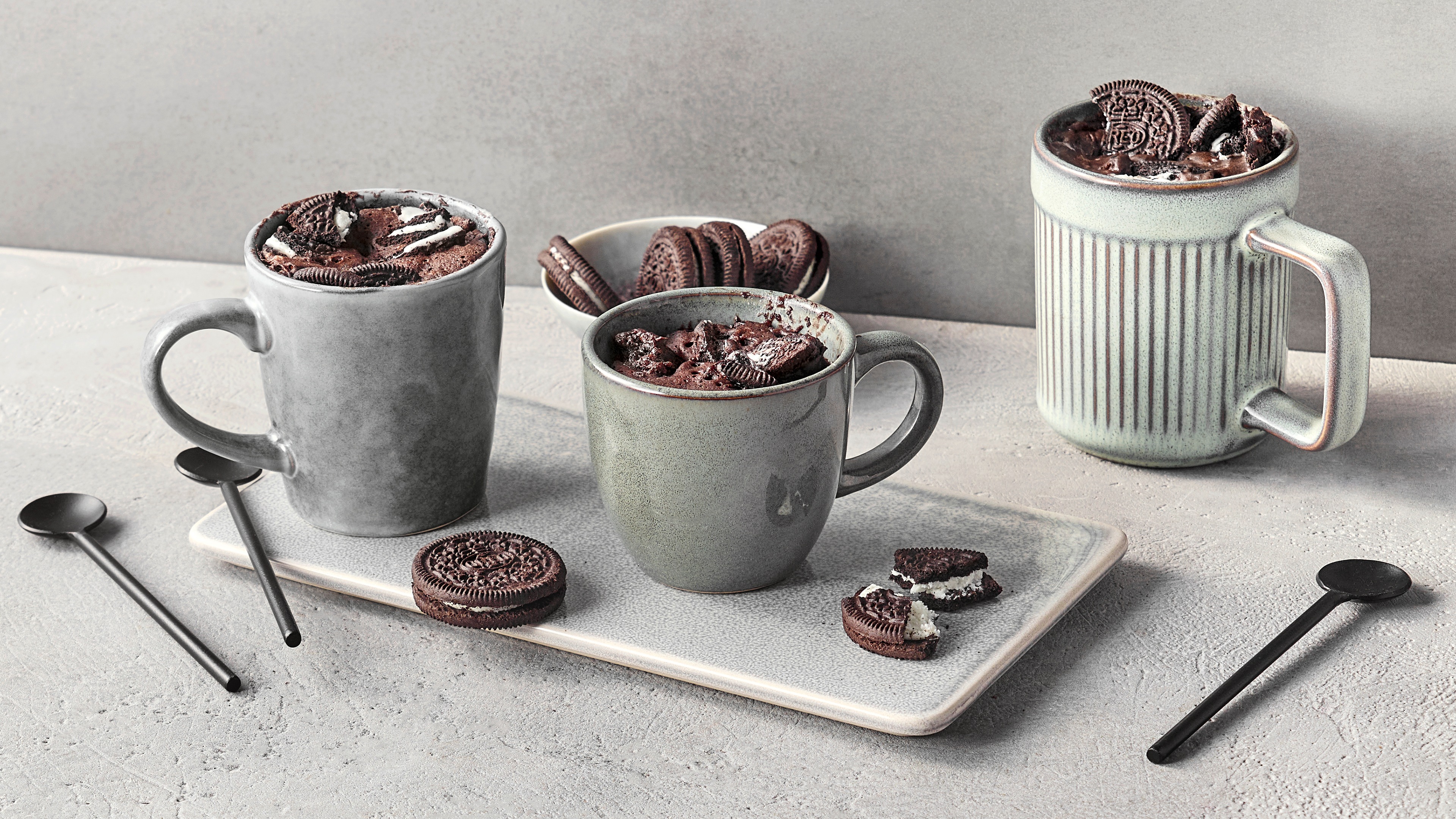 Tassen, gefüllt mit dunkler Creme und zerbröselten Schokokeksen, daneben ein schwarzer Löffel und Kekskrümel.