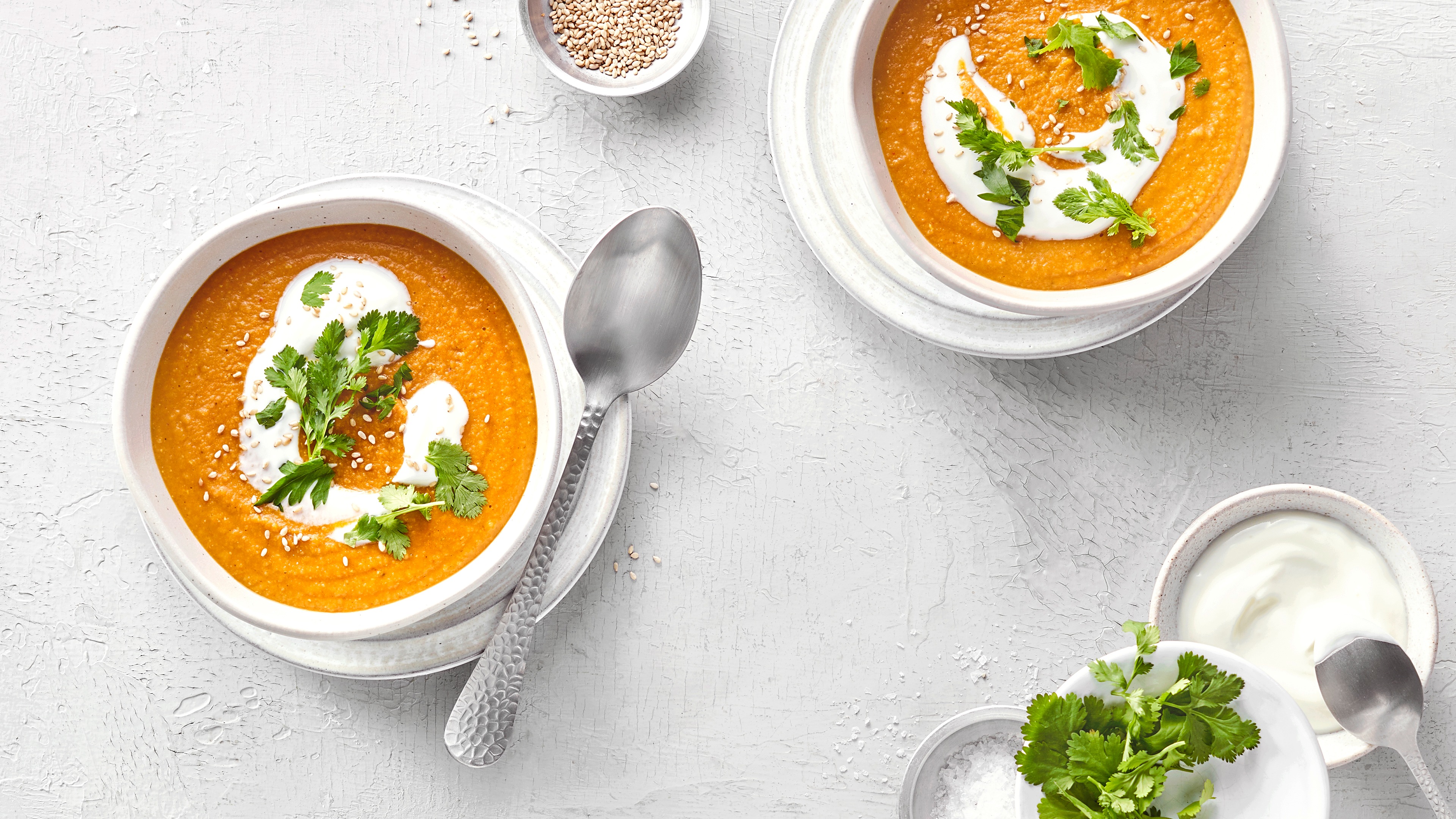 Zwei Schalen mit einer cremigen Linsensuppe, jeweils einem Klecks Joghurtcreme und Petersilie.