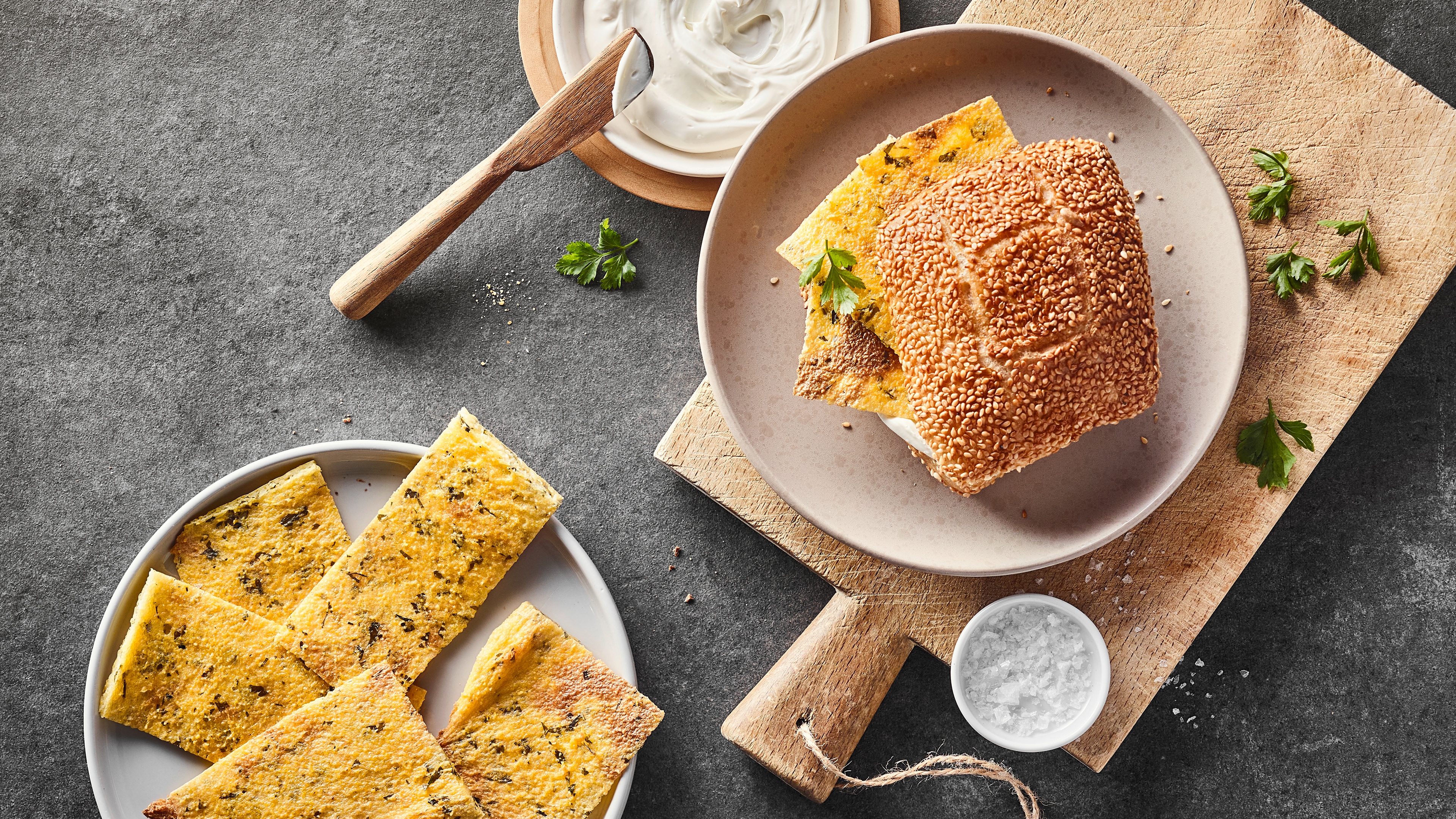 Rezept für Panelle Semesambrötchen mit kross gebratenen Fladen und heller Sauce, garniert mit frischer Petersilie, auf einem runden Teller