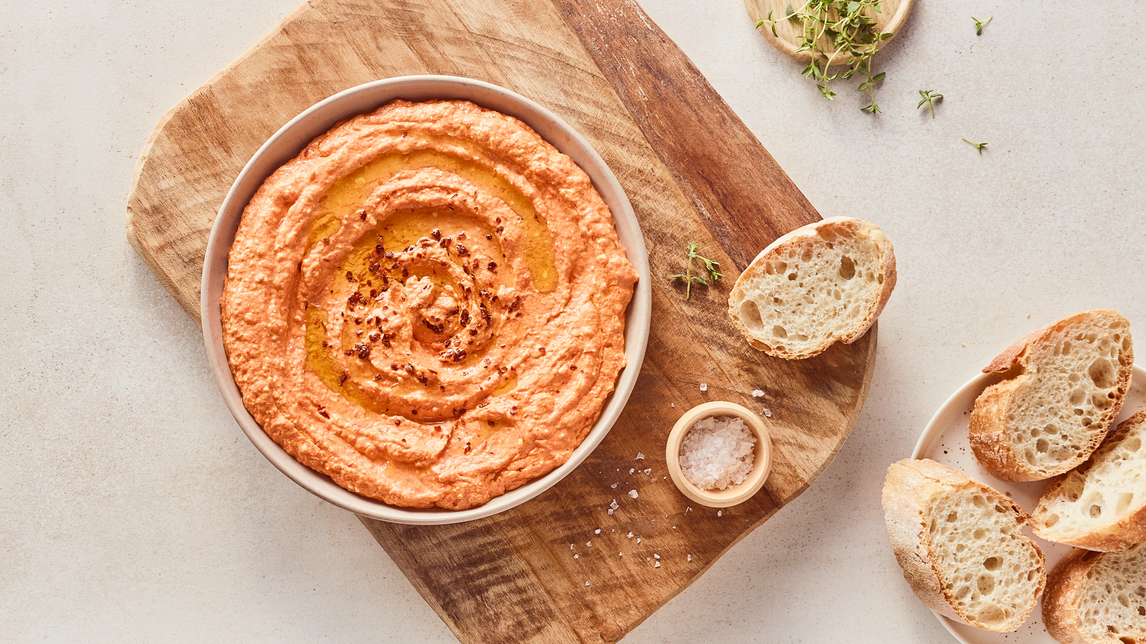 Eine kleine Schüssel mit cremigem hellorangenem Dipp, getoppt mit etwas Öl, daneben ein paar Scheiben frisches Baguette