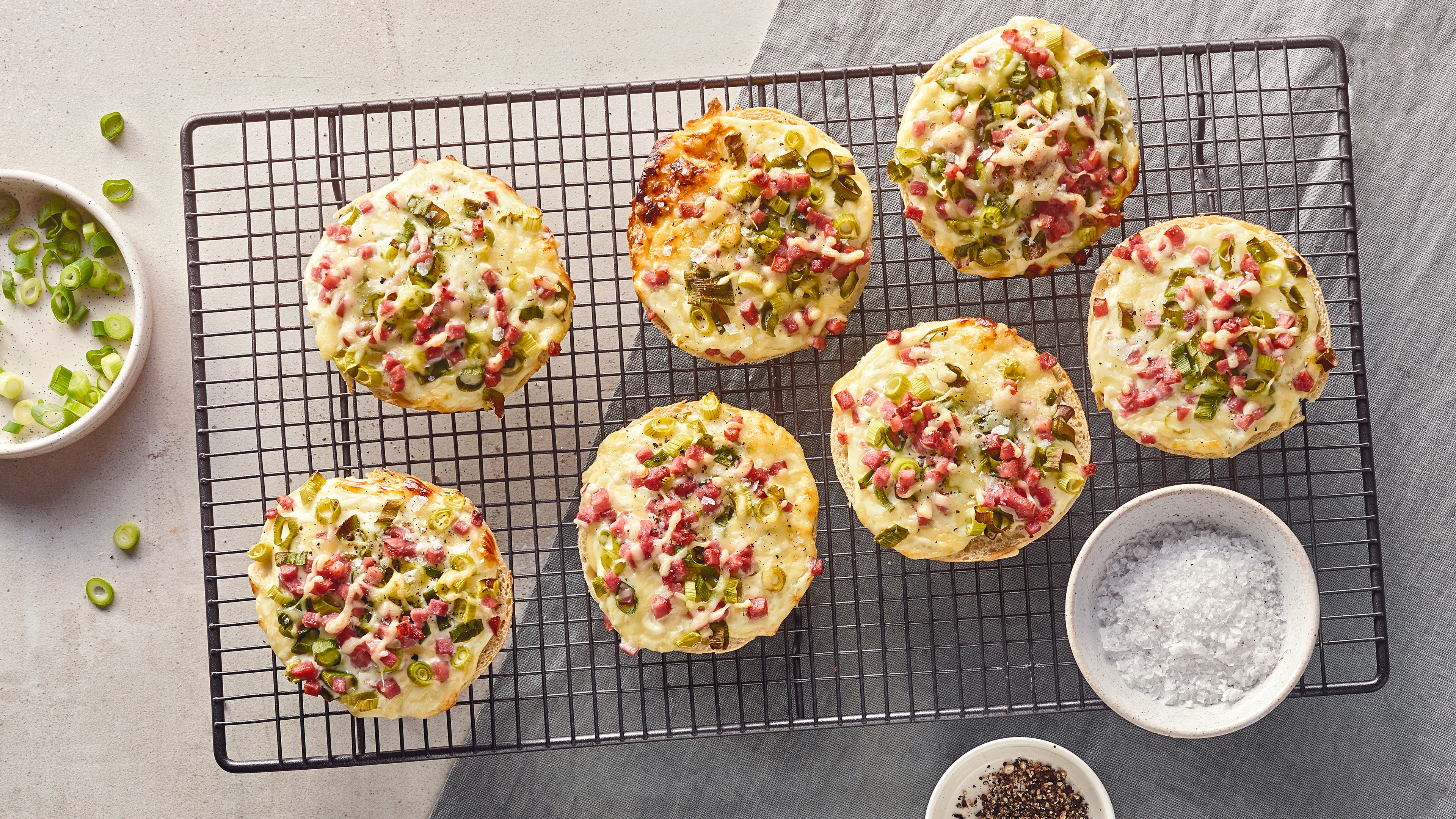 Runde Brötchen, überbacken mit Käse, Schinkenwürfeln und Frühlingszwiebeln, auf einem Backofenrost