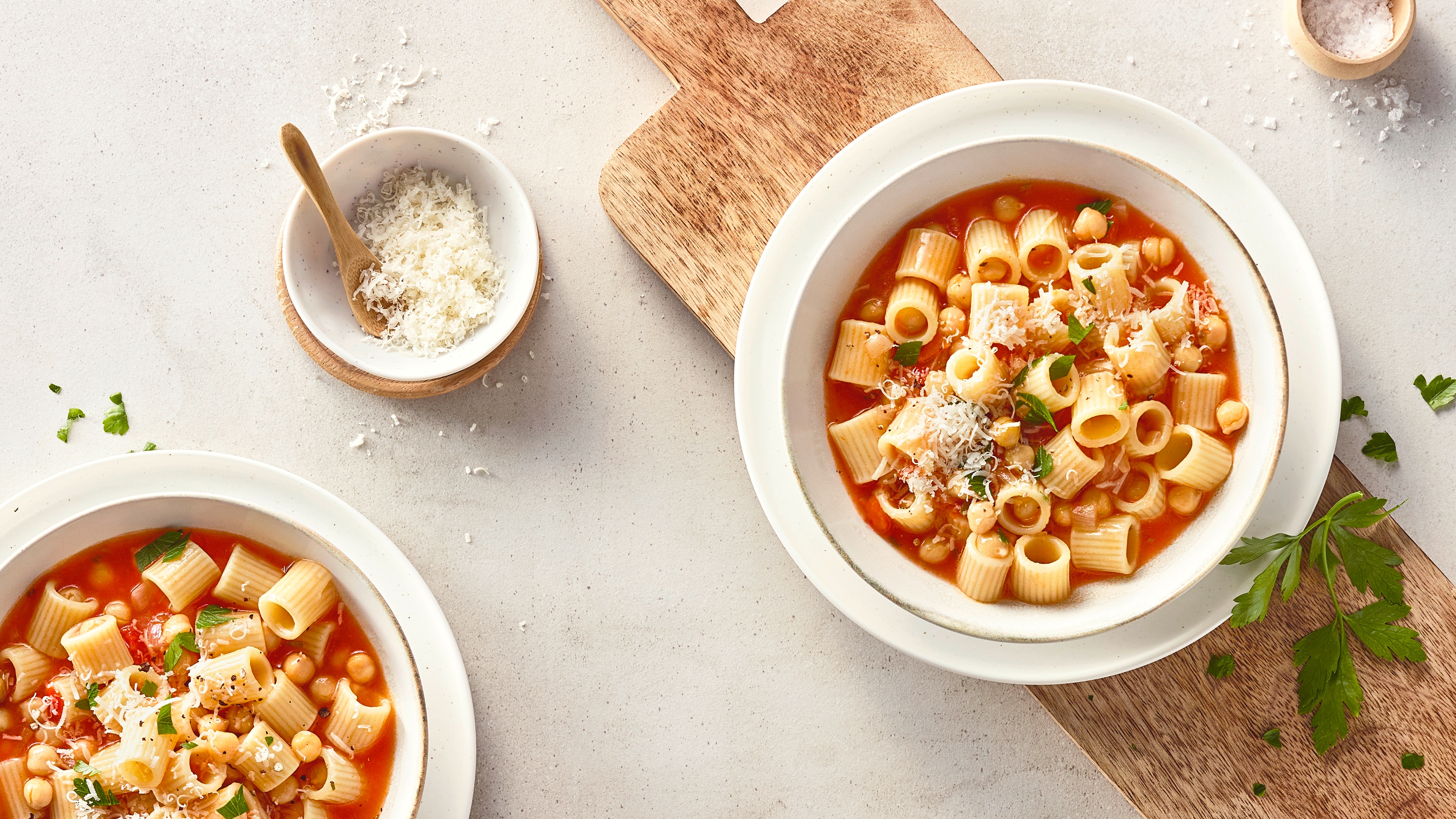 Rezept für Pasta e Ceci Eine Schüssel mit geriffelten, kleinen Nudeln und Kichererbsen in roter Soße, getoppt mit geriebenem Käse und Petersilie