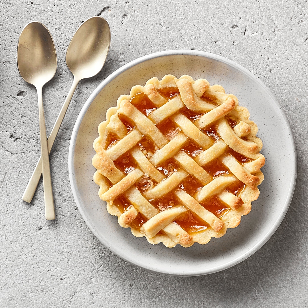 Ein Teller mit einer runden Tarte, gefüllt mit orangefarbener Fruchtfüllung, bedeckt mit einem geflochtenen Teiggitter.