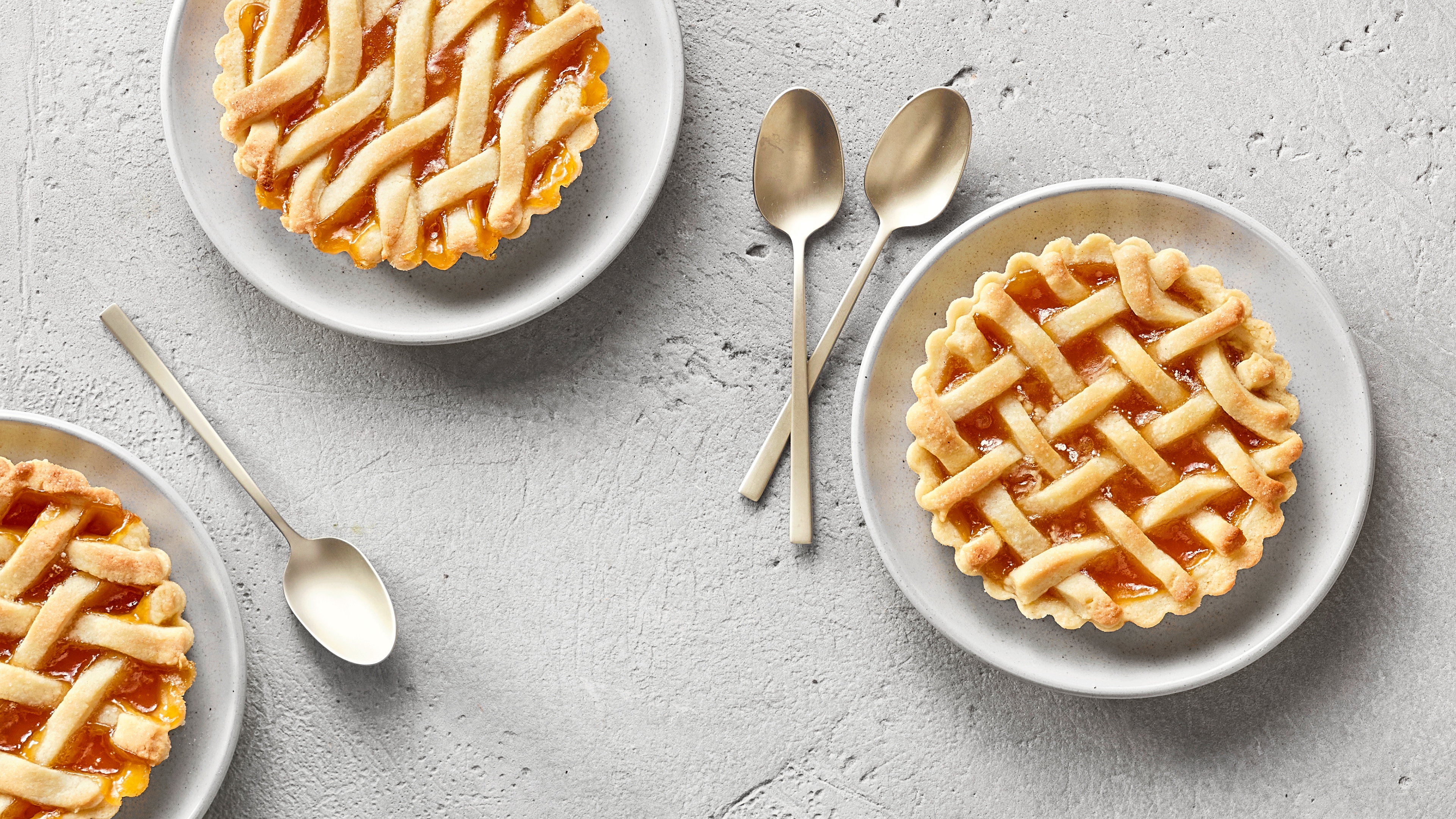 Ein Teller mit einer runden Tarte, gefüllt mit orangefarbener Fruchtfüllung, bedeckt mit einem geflochtenen Teiggitter.