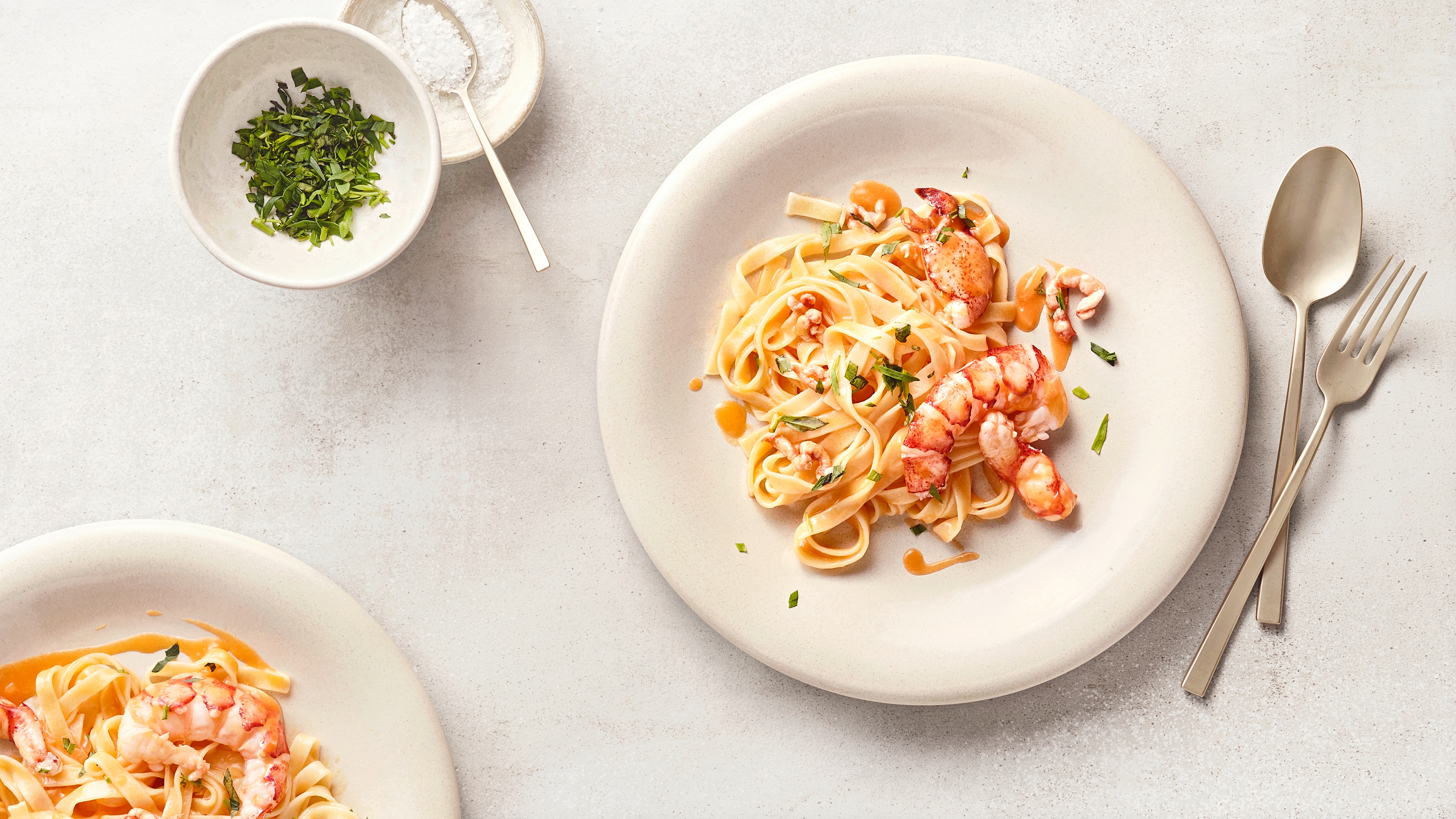Tagliatelle mit Hummerstücken in cremiger Sauce, angerichtet auf einem weißen Teller und mit frischen Kräutern garniert.