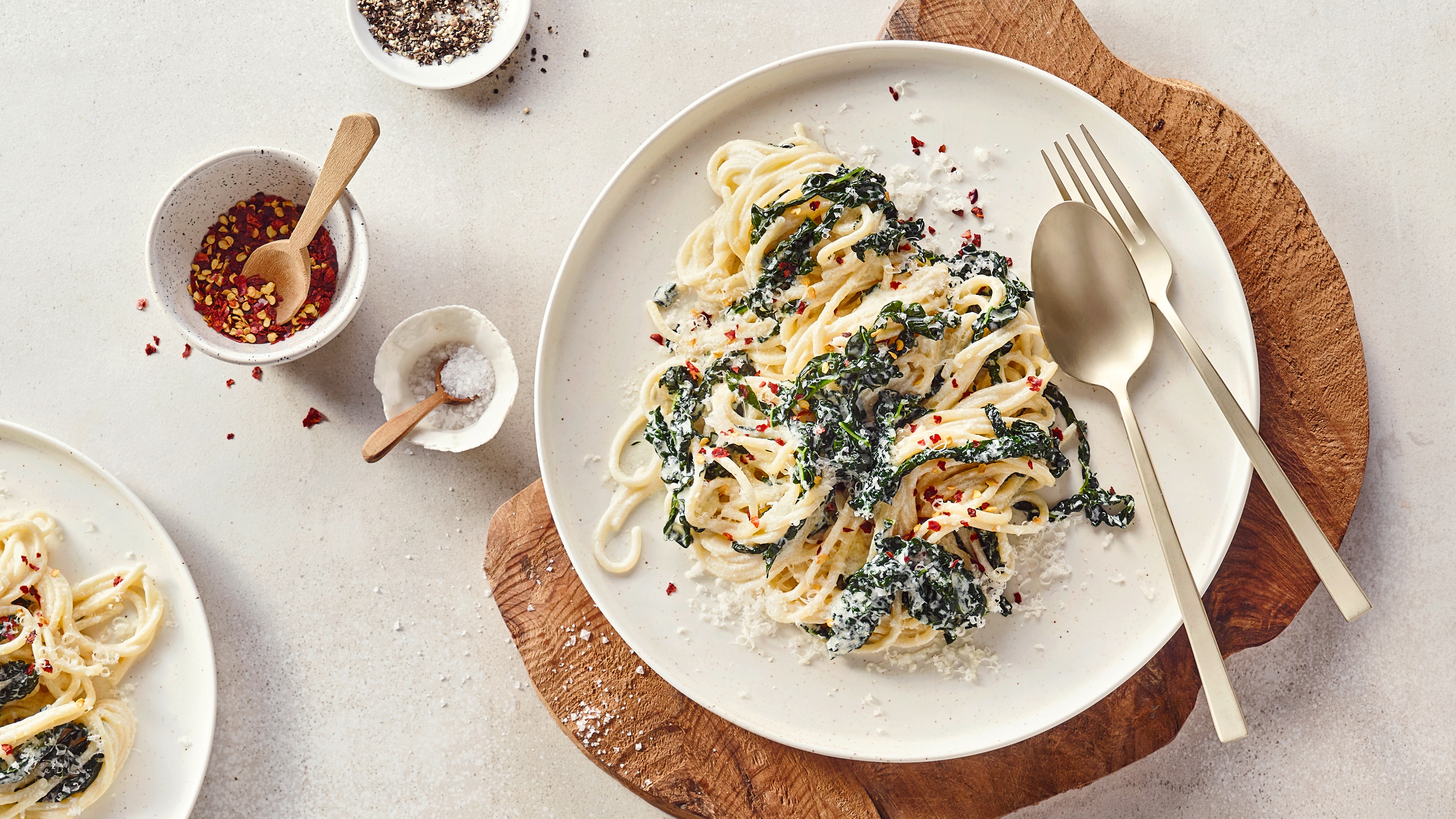 Ein Teller mit Spaghetti in heller Soße, darauf dunkle Blattstücke, geriebener Käse und rote Chiliflocken.