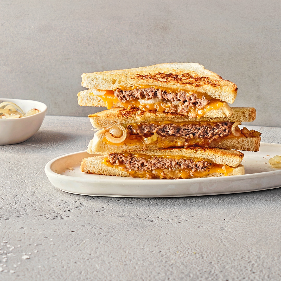 Drei getoastete Sandwichtoast gefüllt mit Hackfleisch, Käse und Zwiebeln auf einem Teller, daneben eine Schale mit Zwiebeln