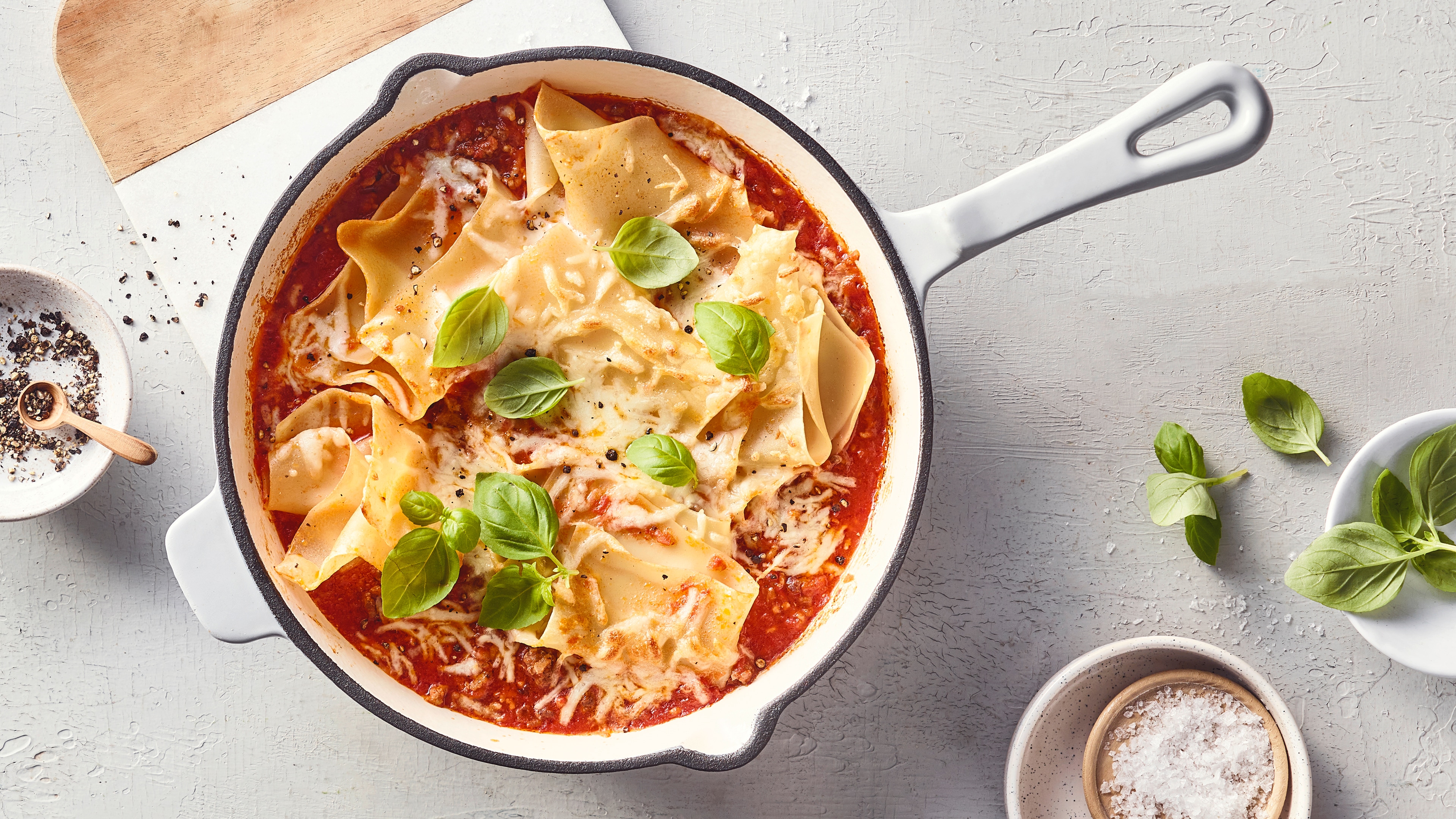 Eine Pfanne mit Lasagneblättern in roter Sauce, bestreut mit geschmolzenem Käse und garniert mit frischen grünen Basilikumblättern