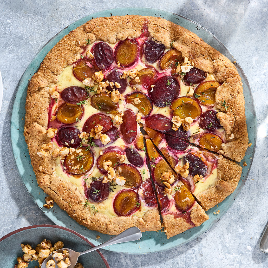 Ein Kuchen mit knusprigem Rand, Pflaumenhälften und Haselnusstücken