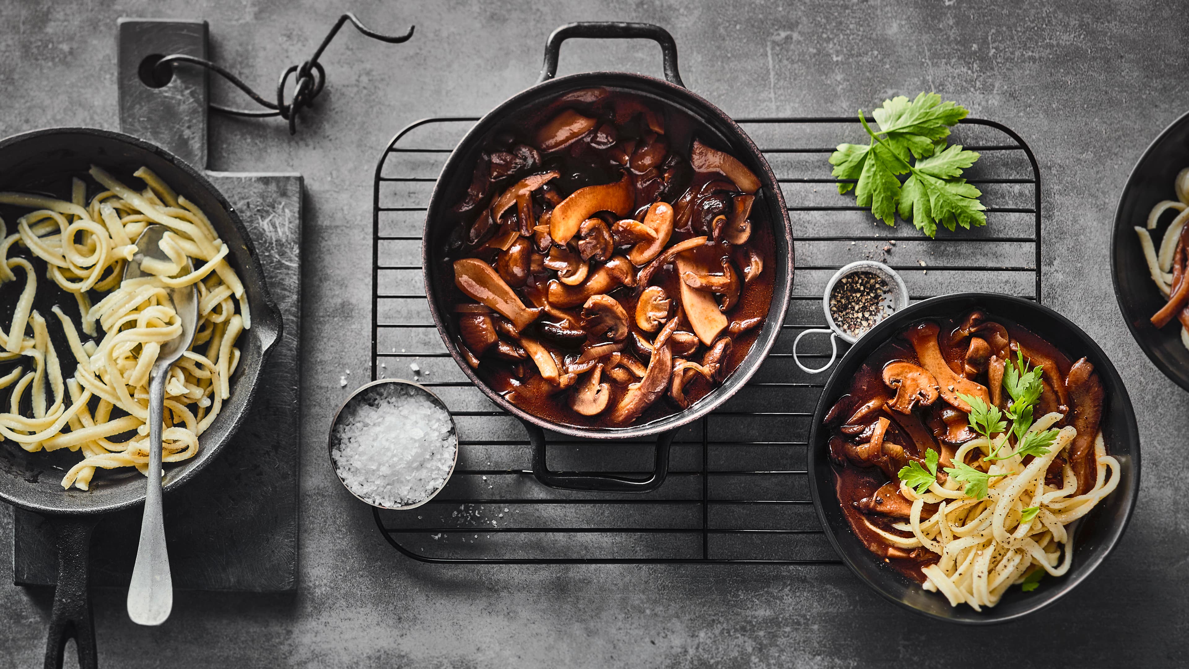 Rezept für würziges Pilzgulasch Eintopfgericht aus Champignons und Kräuterseitlingen in dunkler Soße, getoppt mit Petersilie, in einem gusseisernen Topf.