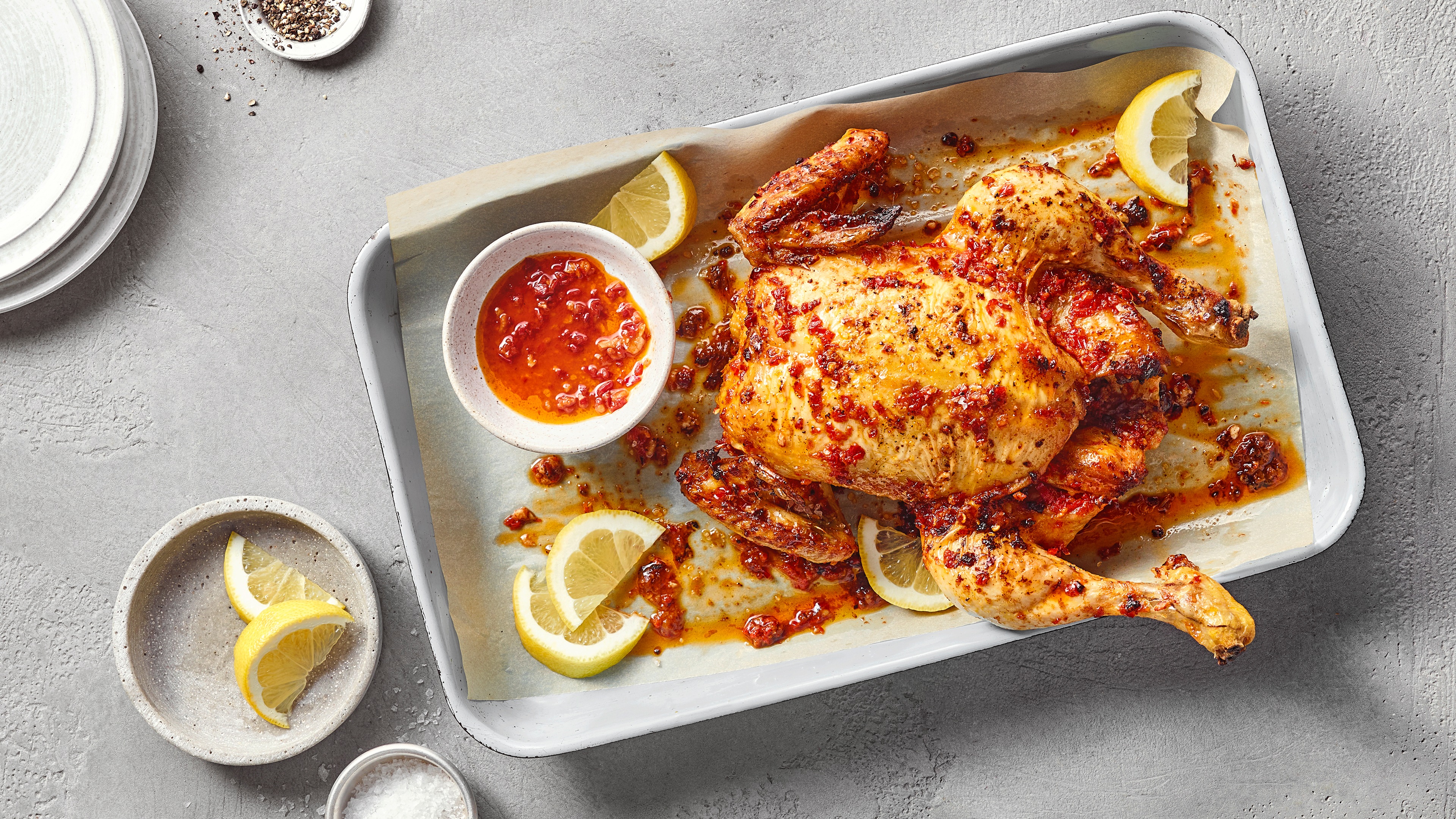 Ein Blech mit einem ganzen gebratenen Hähnchen in roter Gewürzsoße, umgeben von Zitronenspalten und einer Schale roter Soße.