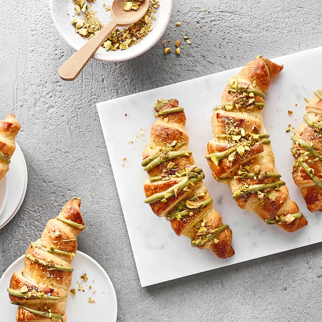 Buttercroissants mit Pistaziencreme‑Füllung, bestreut mit gehackten Pistazien.