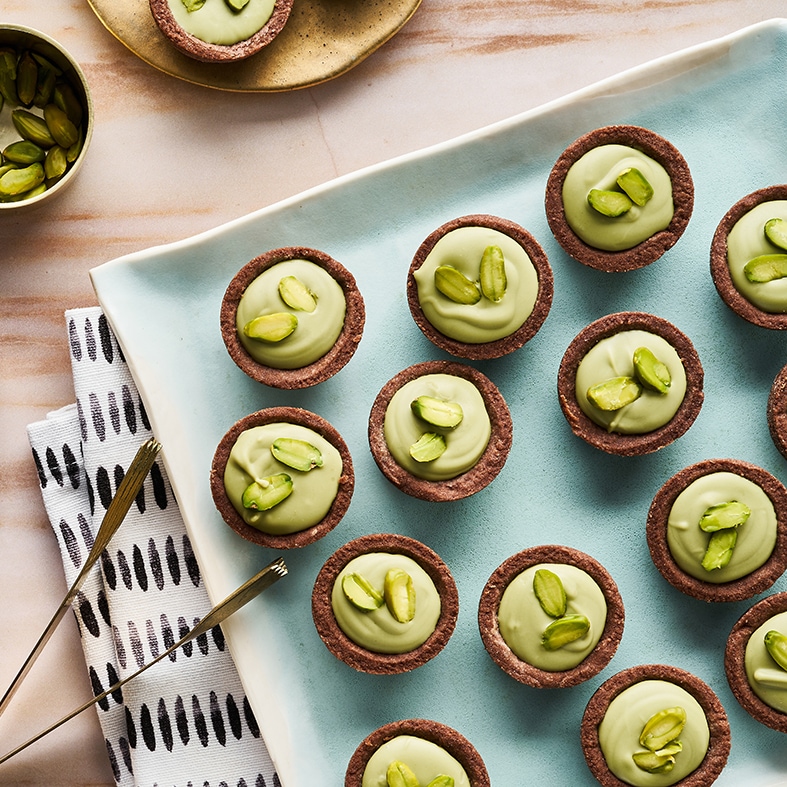 Kleine braune Gebäcktörtchen mit grüner Creme und Pistazien