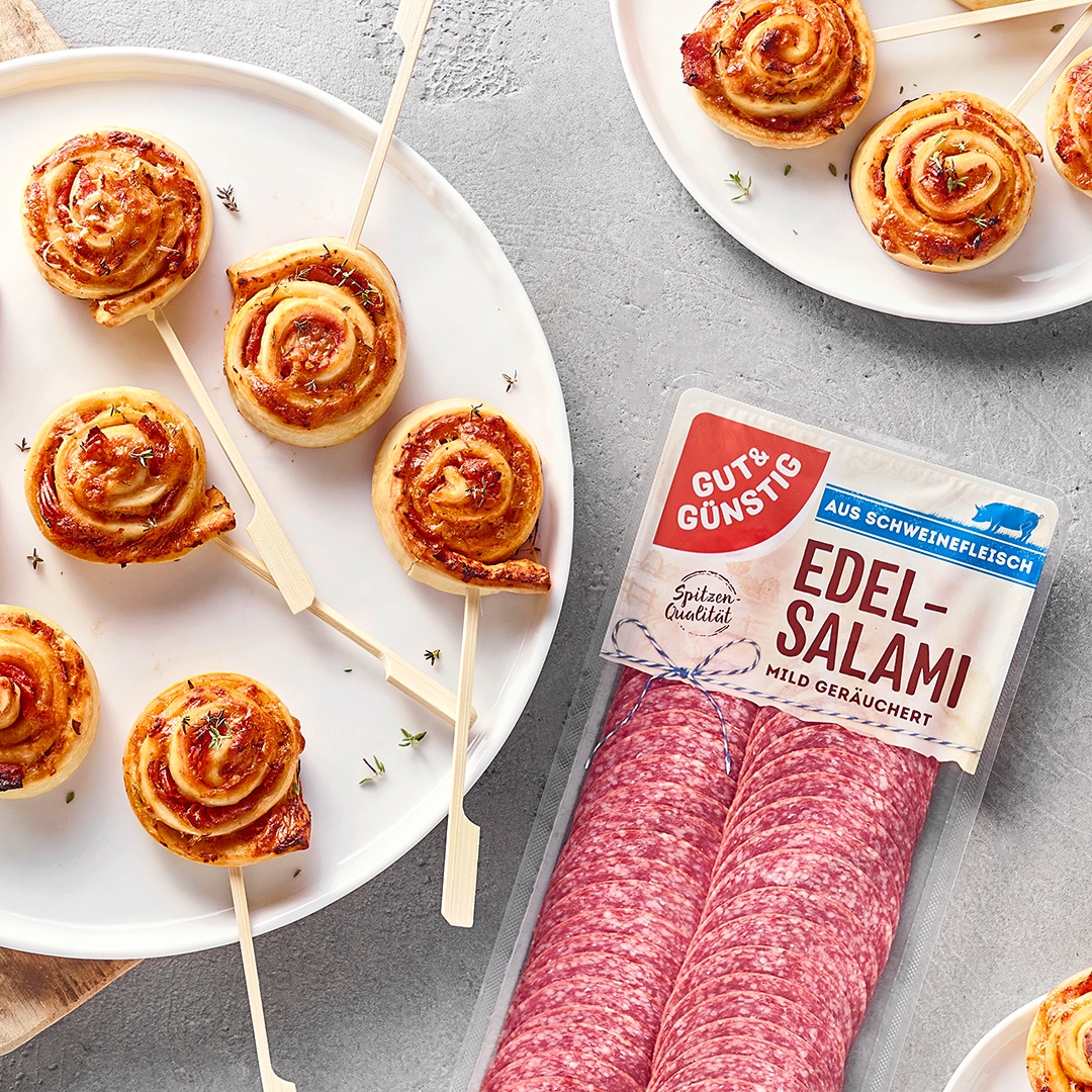 Blätterteig-Schnecken mit Tomatensauce und Salami am Stiel auf einem Servierteller, daneben GUT&GÜNSTIG Edel-Salami.