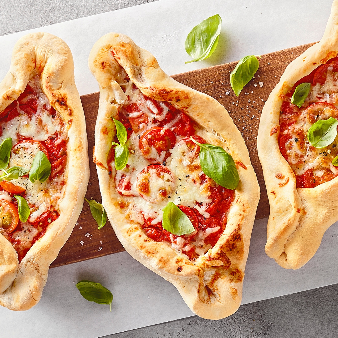 Eine längliche, ovale Pizza mit roter Soße, Tomatenstückchen und geschmolzenem Käse, garniert mit frischen Basilikumblättern