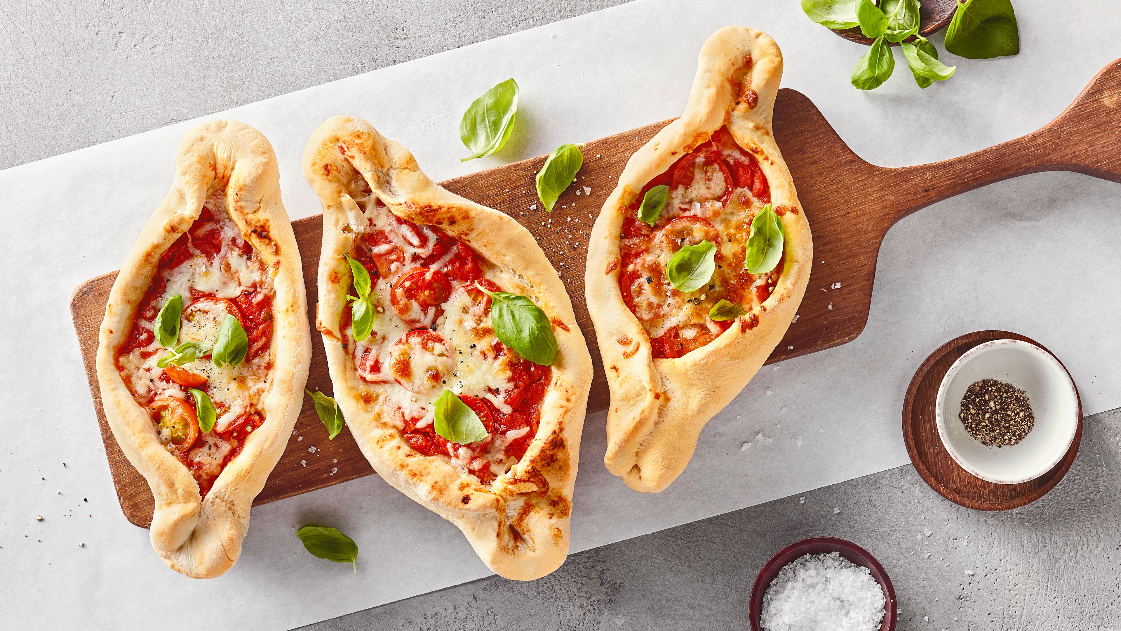 Eine längliche, ovale Pizza mit roter Soße, Tomatenstückchen und geschmolzenem Käse, garniert mit frischen Basilikumblättern