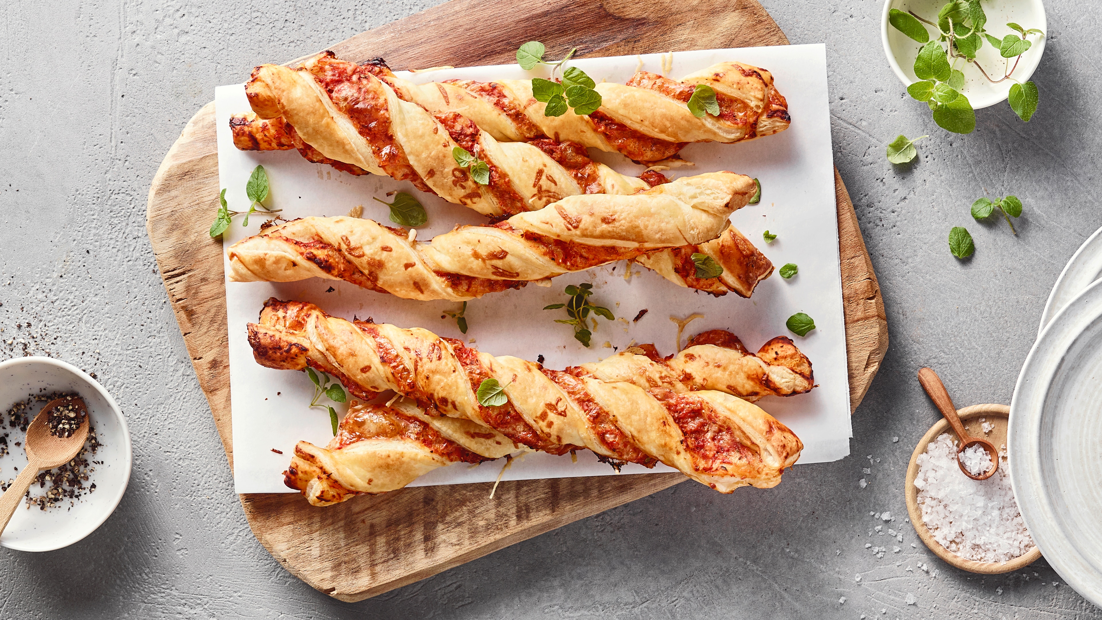 Ein Brett mit gedrehten hellbraunen Teigstangen, gefüllt mit Tomatensauce und garniert mit frischen Kräutern.