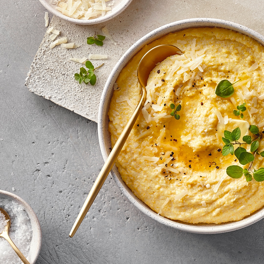Eine Schale mit cremiger Polenta, garniert mit geriebenem Käse, frischen grünen Kräutern, schwarzem Pfeffer und etwas Öl