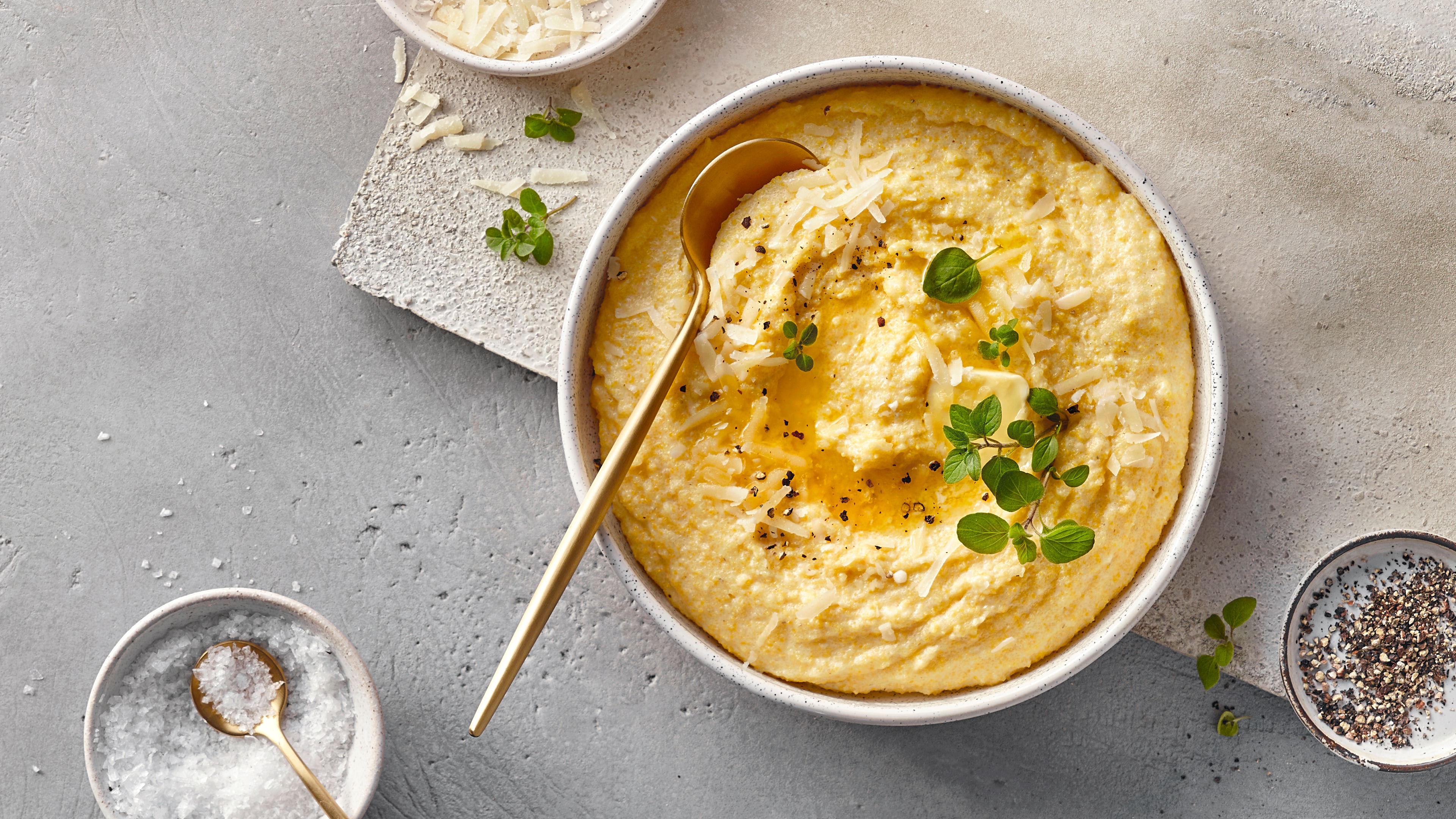 Eine Schale mit cremiger Polenta, garniert mit geriebenem Käse, frischen grünen Kräutern, schwarzem Pfeffer und etwas Öl