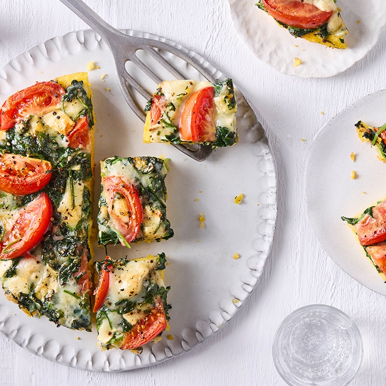 Großer Teller mit in Stücke geschnittener runder Tarte mit Tomatenscheiben und Spinat
