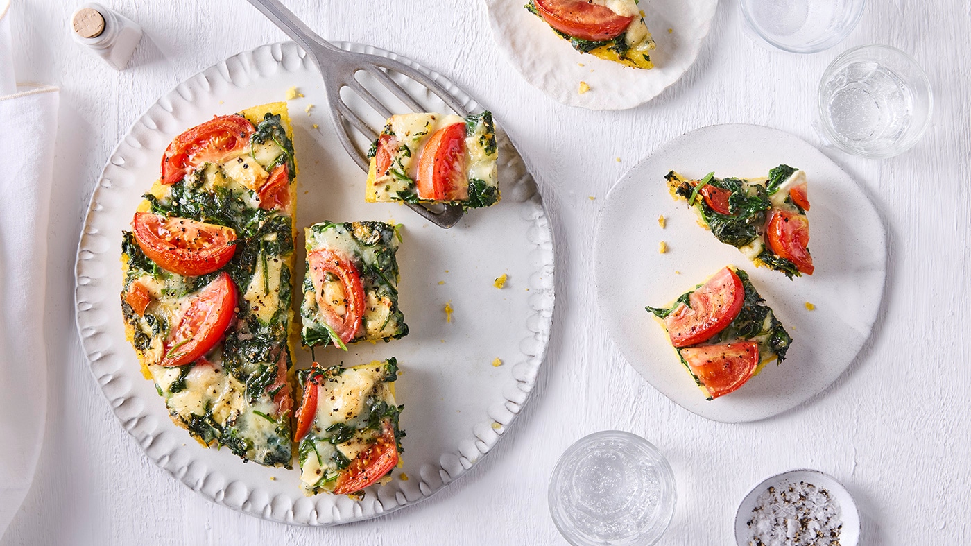 Großer Teller mit in Stücke geschnittener runder Tarte mit Tomatenscheiben und Spinat
