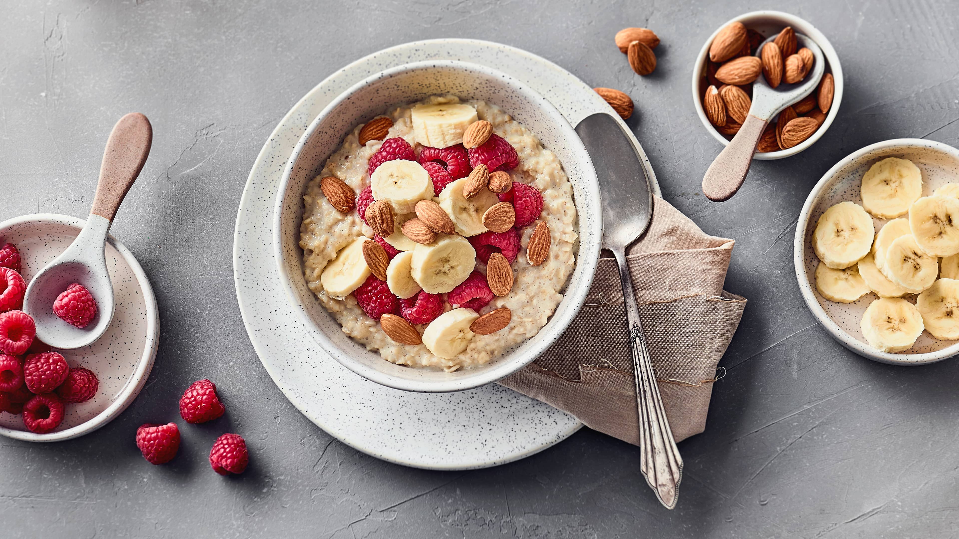 Rezept für Porridge in der Mikrowelle Eine Schale mit cremigem Haferbrei, getoppt mit frischen Himbeeren, Bananen-Scheiben und ganzen Mandeln