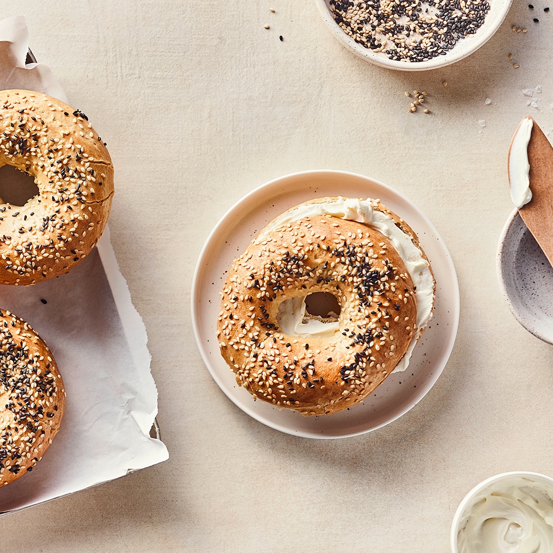 Gelbgold gebacknene Bagel mit weißem und schwarzem Sesam und cremigem Frischkäse, auf einem runden Teller